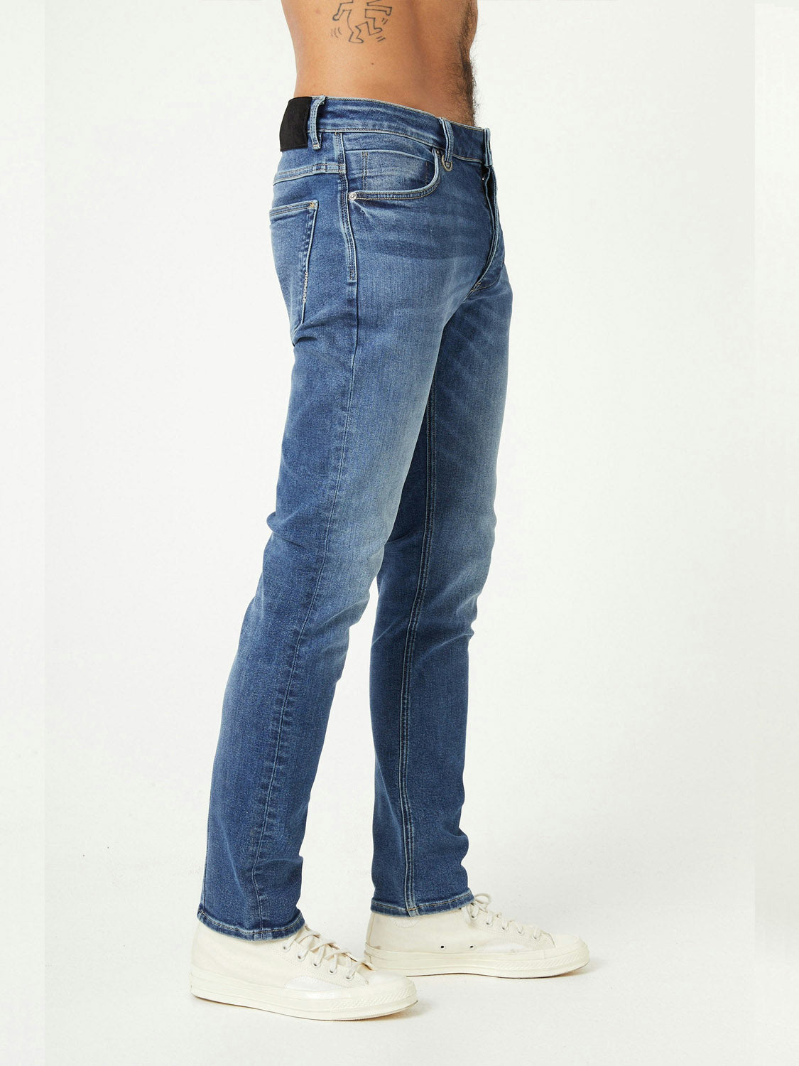 A person is shown from the waist down wearing Neuw Lou Slim Destination jeans and white sneakers, standing sideways against a plain white background.