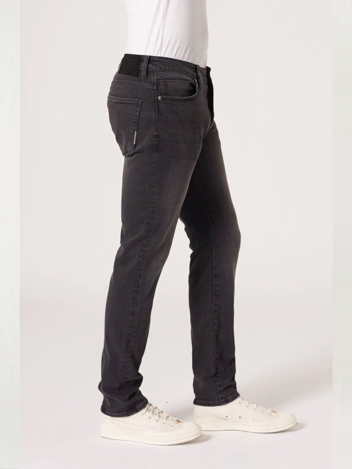 A person models Neuw’s Lou Slim Moonshake jeans in classic black, styled with a white shirt and sneakers against a plain background. Shown in profile with relaxed hands, these slim-fit jeans achieve a sleek, modern aesthetic.