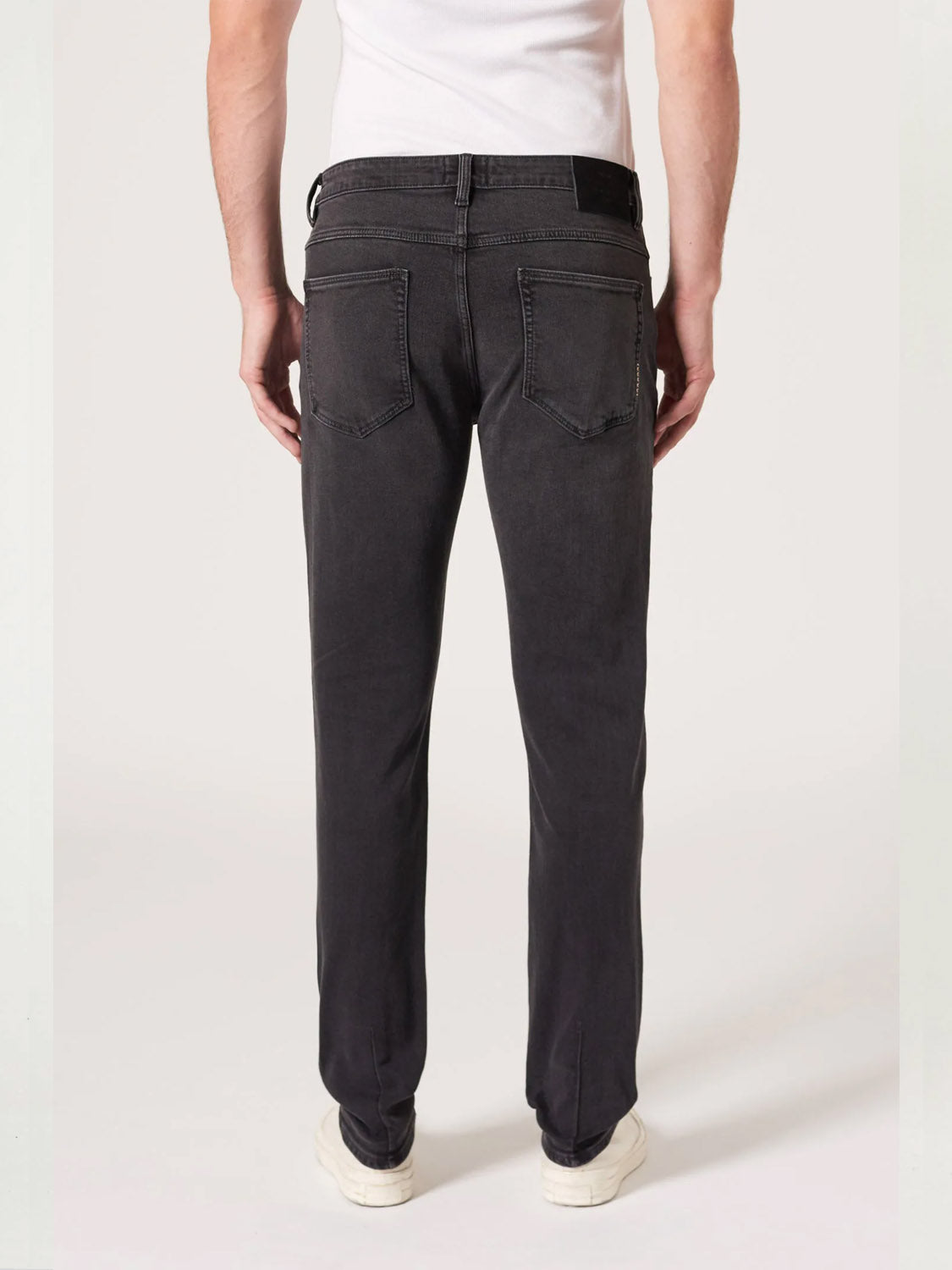 A person in a white t-shirt, Neuw Lou Slim Moonshake jeans, and white shoes stands facing away from the camera against a plain light background.