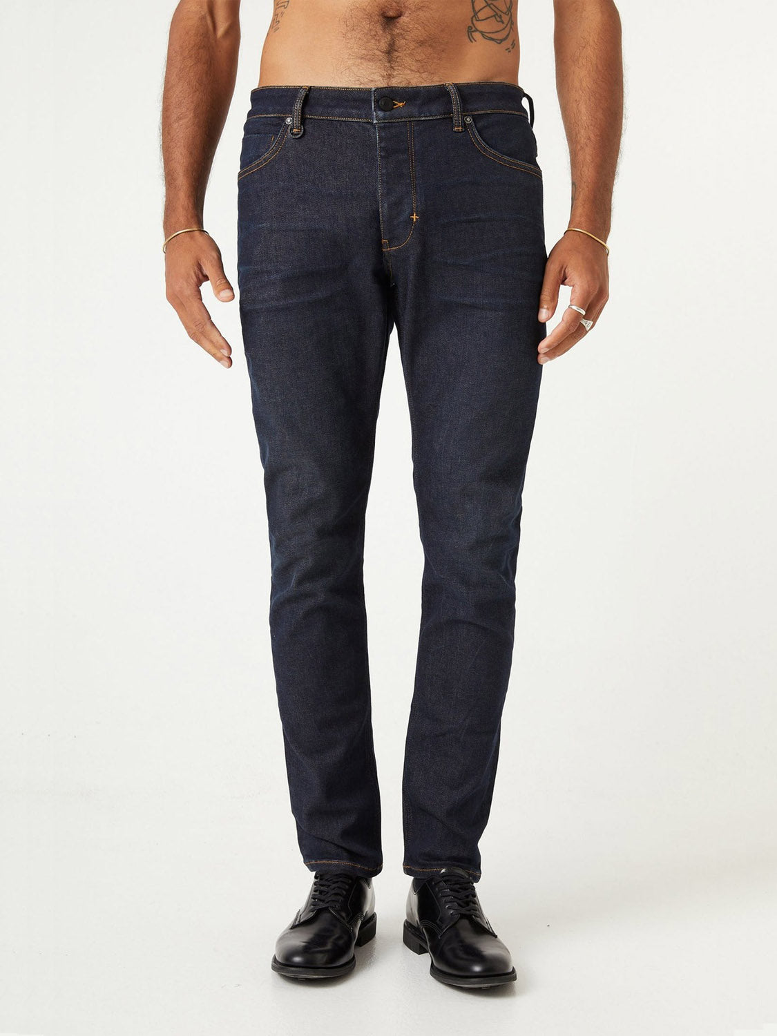 A man stands against a plain background, wearing ID Menswear's Lou Slim - Typecast jeans in dark blue with black dress shoes. His upper body is partially out of frame, and his arms hang relaxed by his sides.