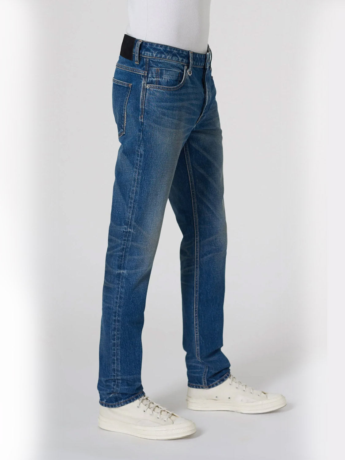 A person models the Neuw Lou Slim Seventeen jeans, crafted from premium stretch denim, paired with white sneakers. Shown from waist down in a side view against a plain light background.