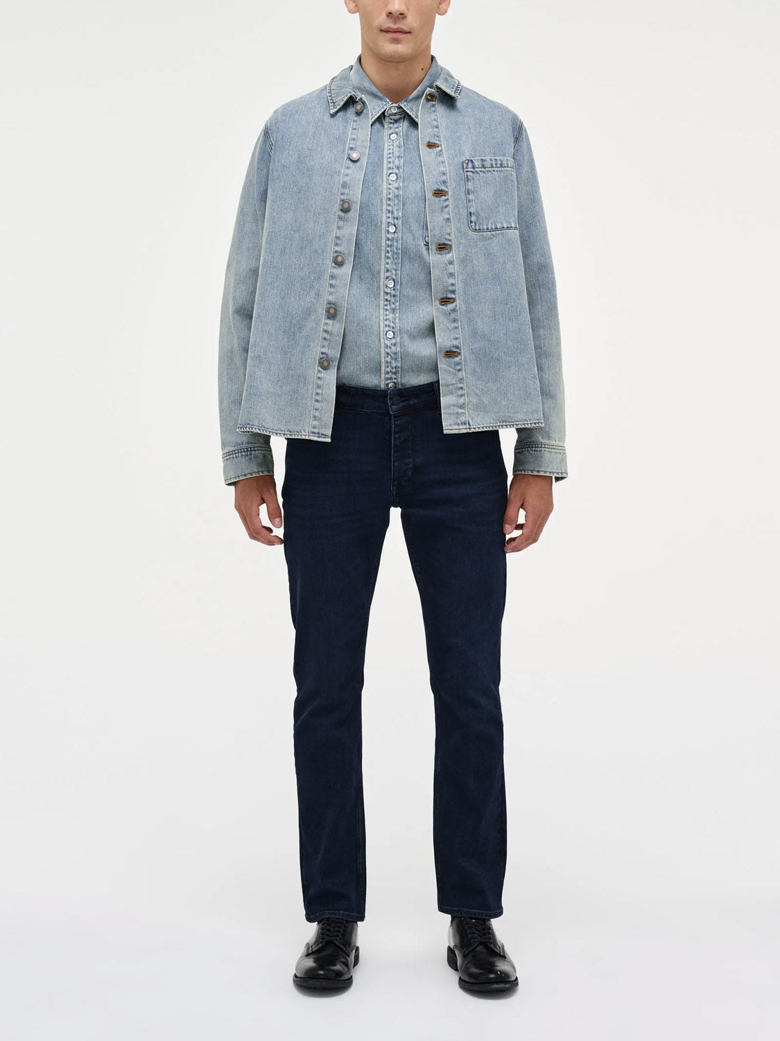 A man faces forward wearing the Neuw Lou Straight Silent Water indigo jeans with a light blue denim jacket, a matching denim shirt, and black shoes against a plain white background.
