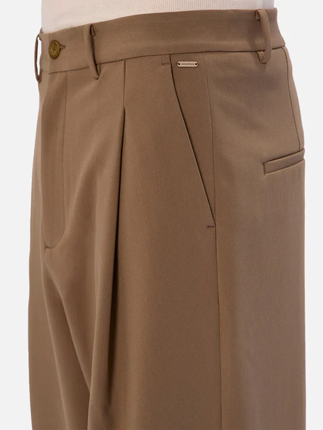 Close-up of a person wearing Industrie Lusso Loose Fit Pant in light brown stretch fabric, detailed with a front button, belt loops, side pockets, and a small metallic brand tag near the right pocket.