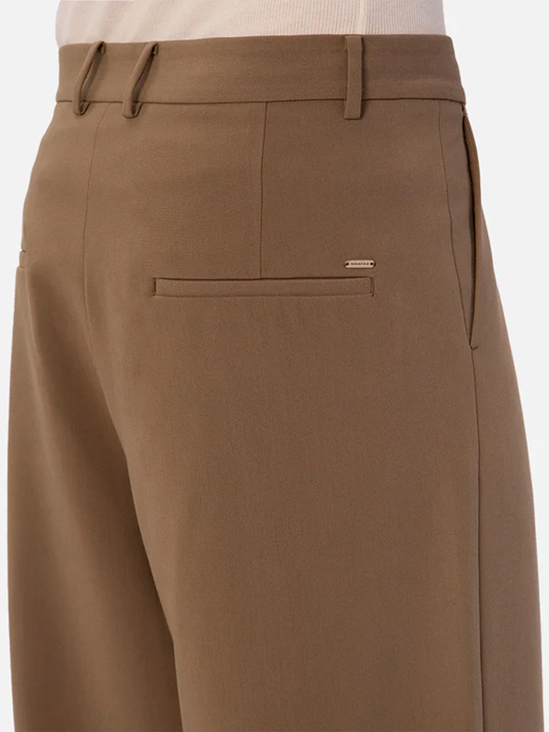 A close-up of a person wearing the Lusso Loose Fit Pant by Industrie, high-waisted brown tailored pants with belt loops and a flat front pocket, paired with a tucked-in beige top.