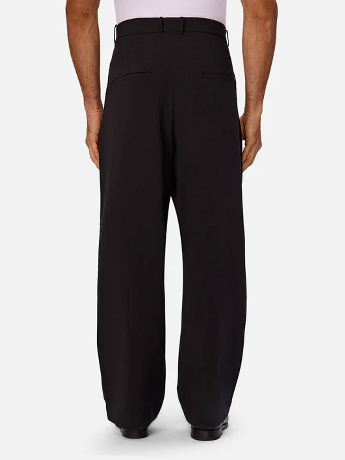 A person is shown from the back, standing against a plain light background, wearing Industrie’s Lusso Loose Fit Pant in high-waisted black with a wide-leg relaxed fit and a white shirt.