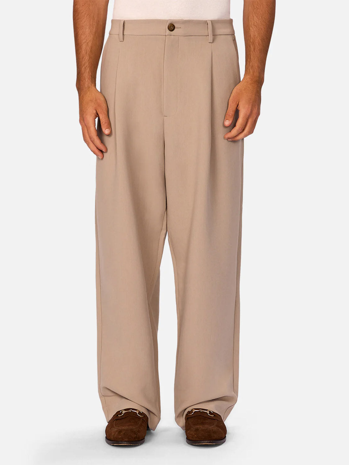 A person in Industrie’s Lightweight Classic Lusso Pant - Stone—high-waisted, wide leg pants—paired with brown loafers stands against a plain light backdrop. Only their lower torso and legs are visible.