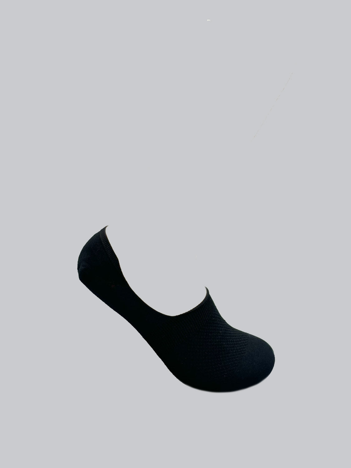 A solitary M1 No Show Sock by ID Menswear, in black and crafted from textured combed cotton, sits against a light gray backdrop. It comfortably covers the foot without reaching the ankle, ideal for low-cut shoes.
