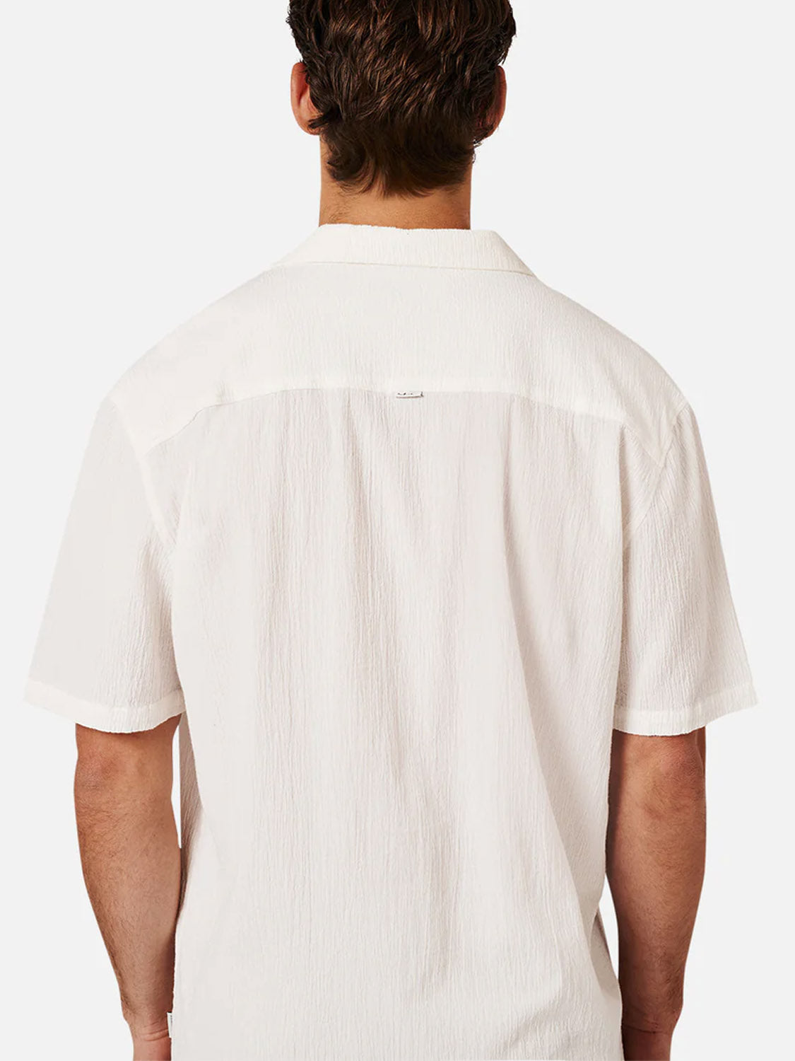 A person with short brown hair is seen from behind, modeling the Industrie Magna Short Sleeve Shirt—an oversized, textured white shirt—against a plain white background.