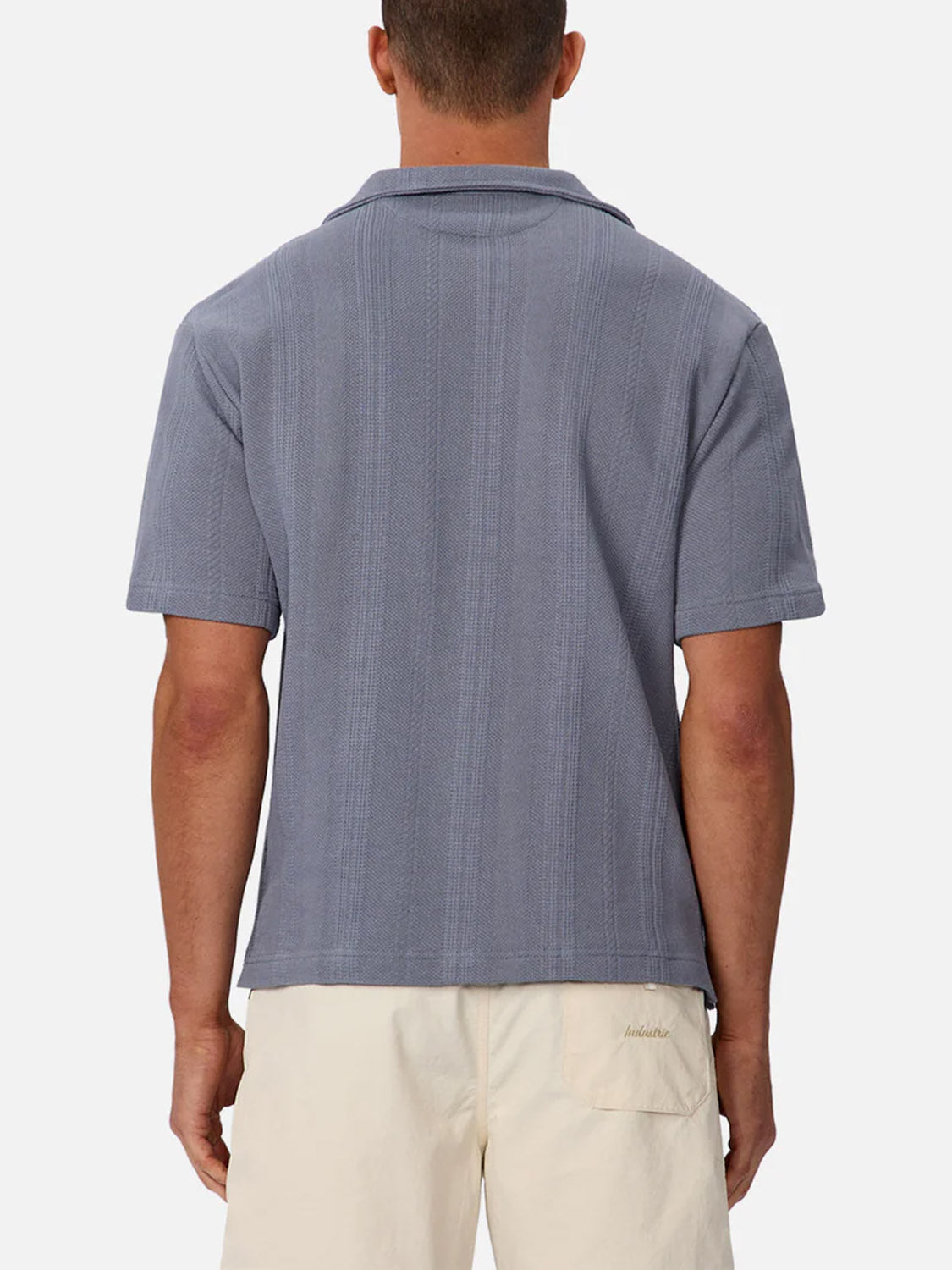 A man is seen from behind wearing the Industrie Malaga Short Sleeve Shirt in light blue and cream-colored shorts, set against a plain light background.