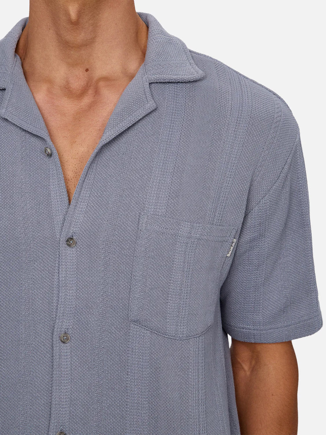 A person wearing the Industrie Malaga Short Sleeve Shirt in textured light gray, featuring a camp collar, short sleeves, and chest pocket, shown from shoulders to mid-torso against a plain background.
