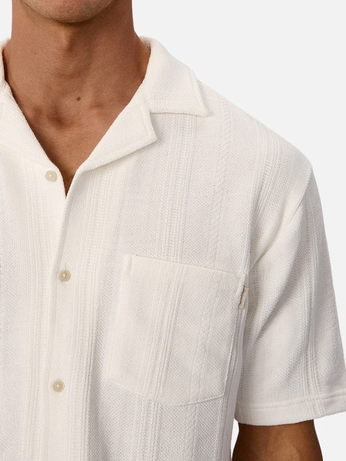 A person wears the Industrie Malaga Short Sleeve Shirt, featuring a white textured finish, camp collar, and chest pocket, shown from shoulders to upper torso against a plain background.