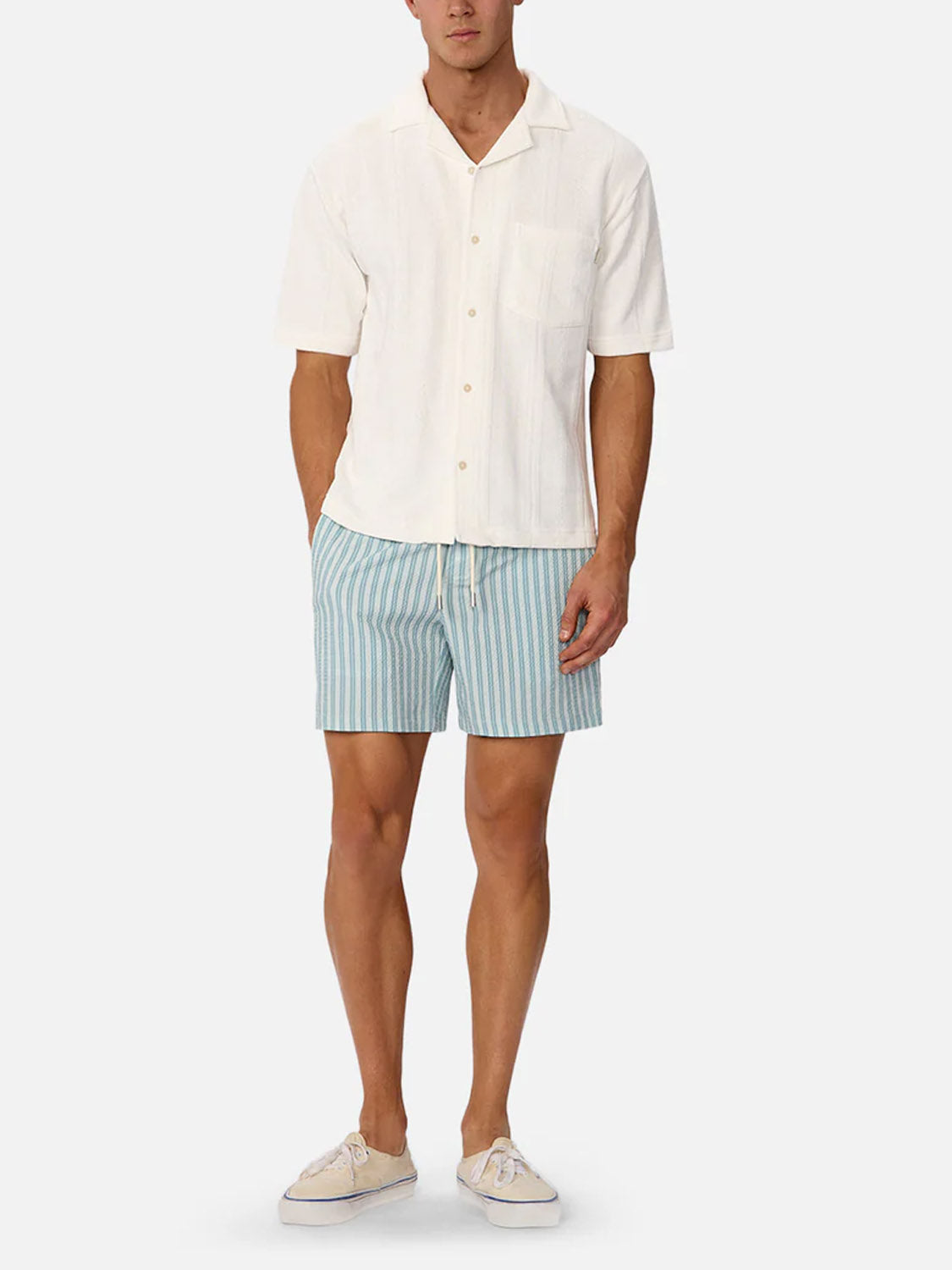 A man wearing the Industrie Malaga Short Sleeve Shirt, light blue and white striped shorts, and light-colored sneakers stands against a plain white background.