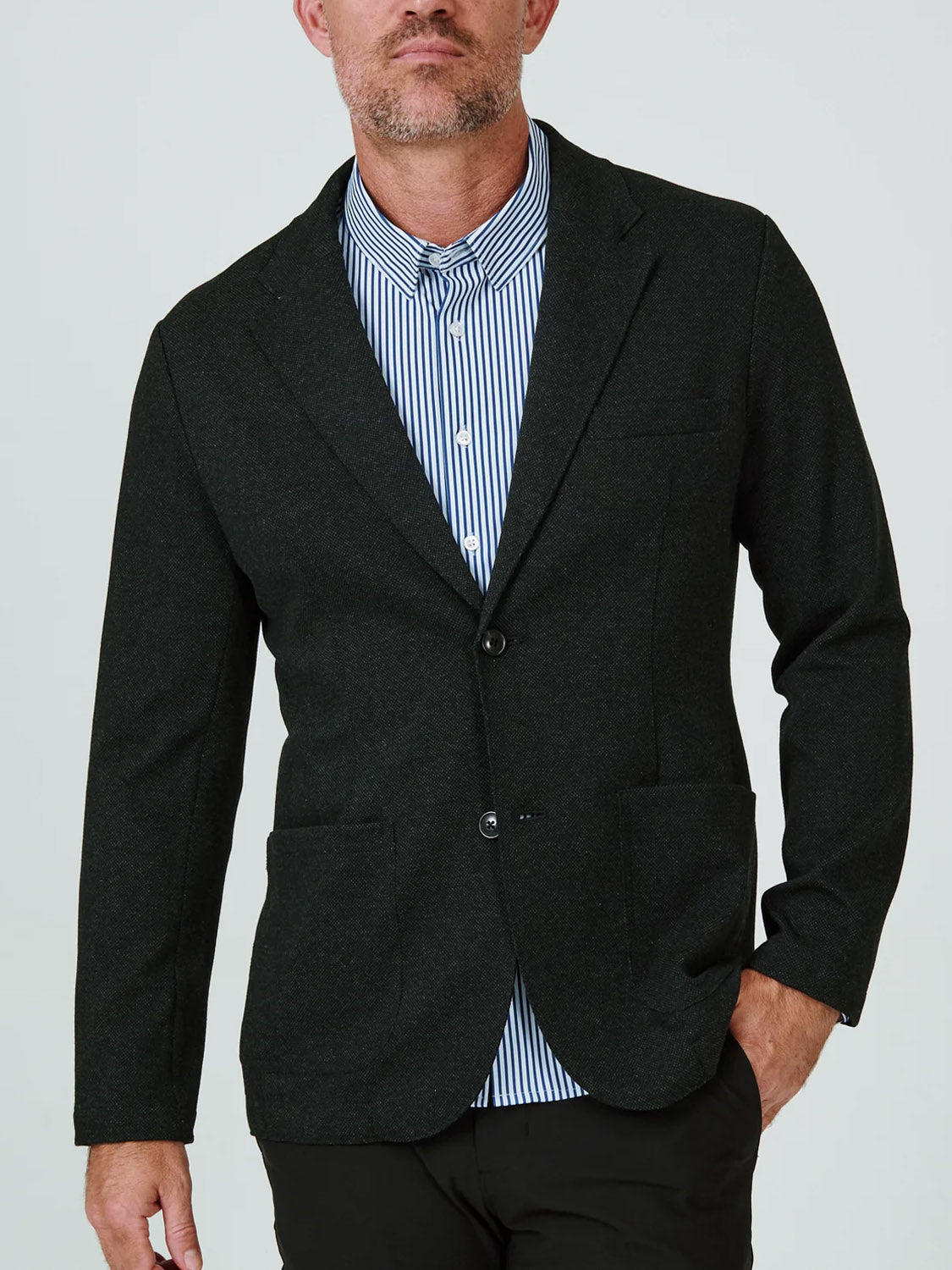 A man models the 7 Diamonds Generation Malibu Blazer over a blue and white striped shirt with black pants—all essentials from the 7 Diamonds collection—crafted from a unique fabric blend, set against a plain light background.