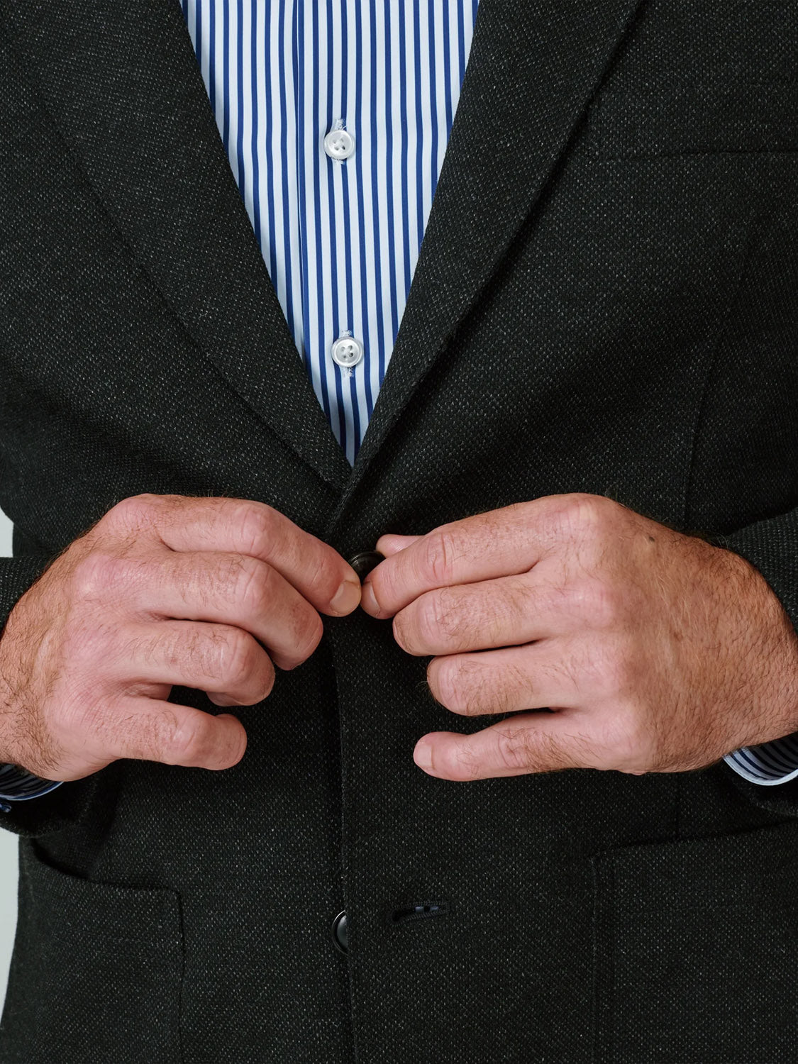 A person wearing the 7 Diamonds Generation Malibu Blazer is buttoning the front of their jacket, showcasing this key wardrobe essential with focus on their hands and torso.