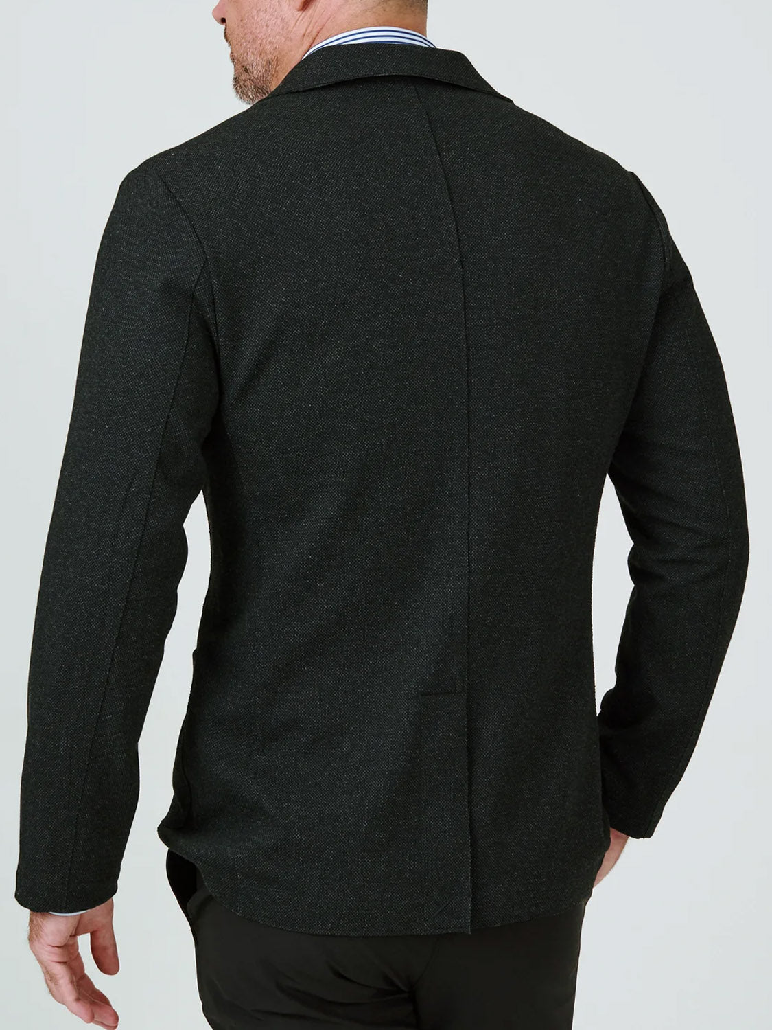 A man is seen from the back in the 7 Diamonds Generation Malibu Blazer with long sleeves and black pants, his head turned slightly left and his left hand by his side.