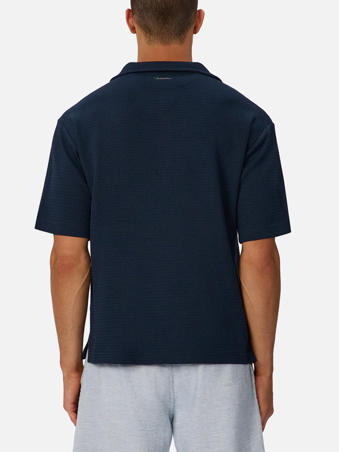 A man is seen from behind wearing The Malibu Short Sleeve Shirt by Industrie with light gray shorts, standing against a plain white background.