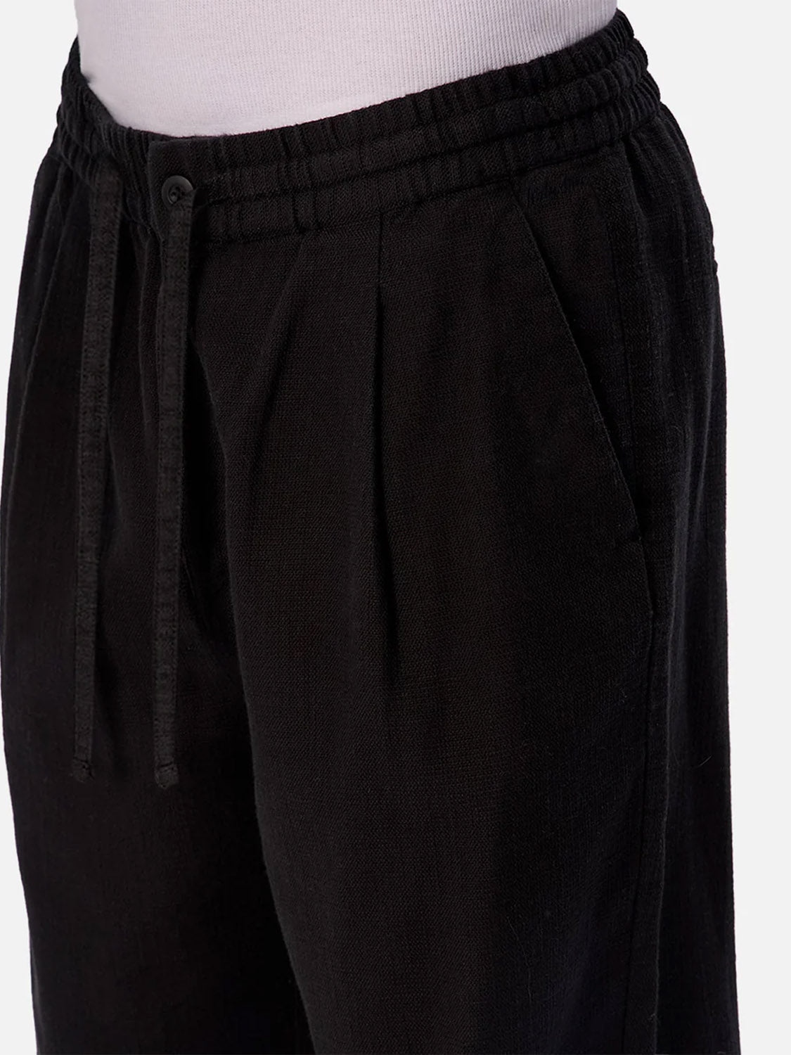 Close-up of a person wearing Industrie’s The Relaxed Mallorca Pant—black cotton drawstring pants with an elastic waistband and pleated front—styled with a light-colored tucked-in top.