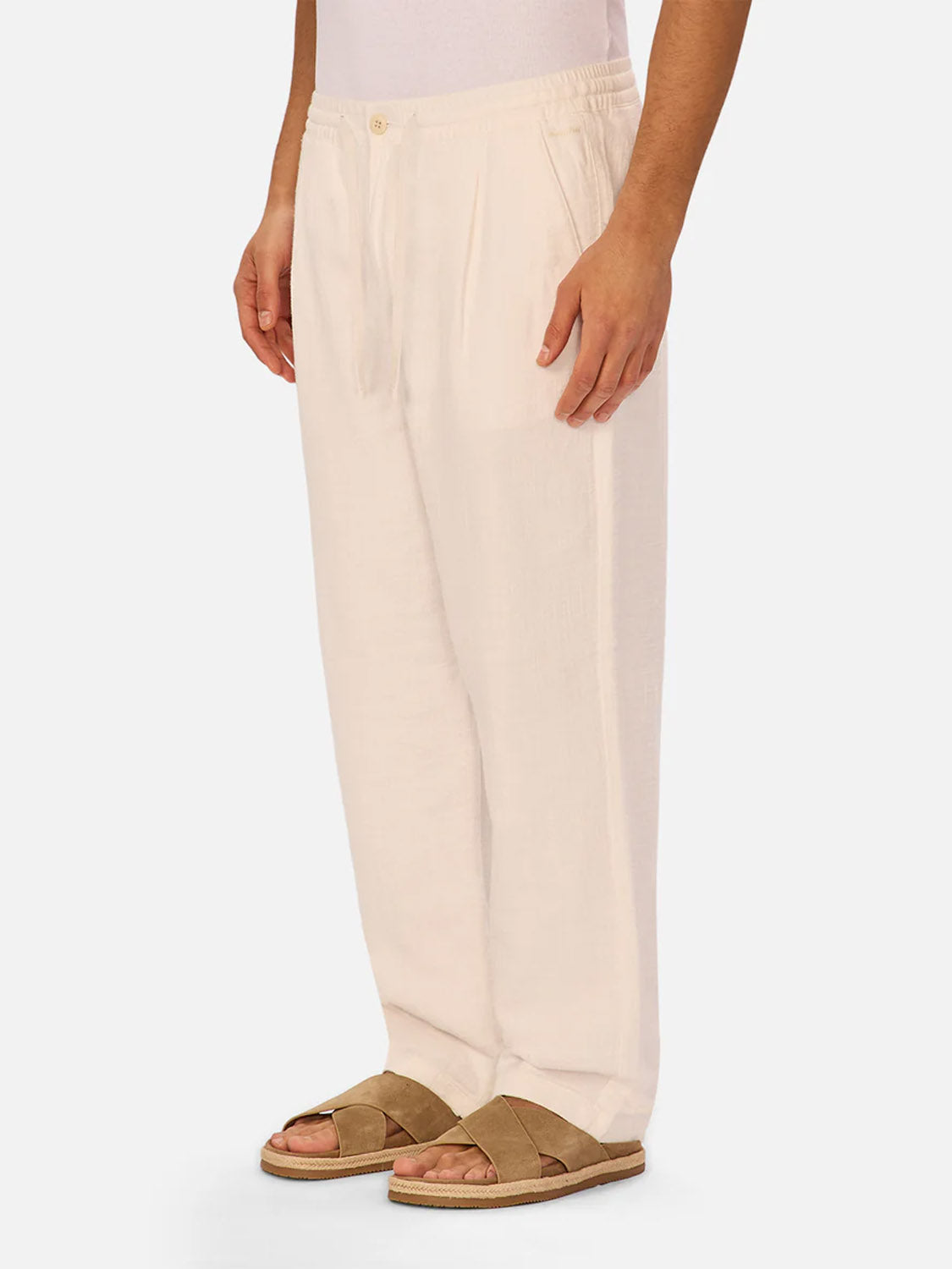A person’s lower half is shown wearing Industrie’s The Relaxed Mallorca Pant in a relaxed fit, made from breathable cotton, paired with tan sandals, against a plain white background.