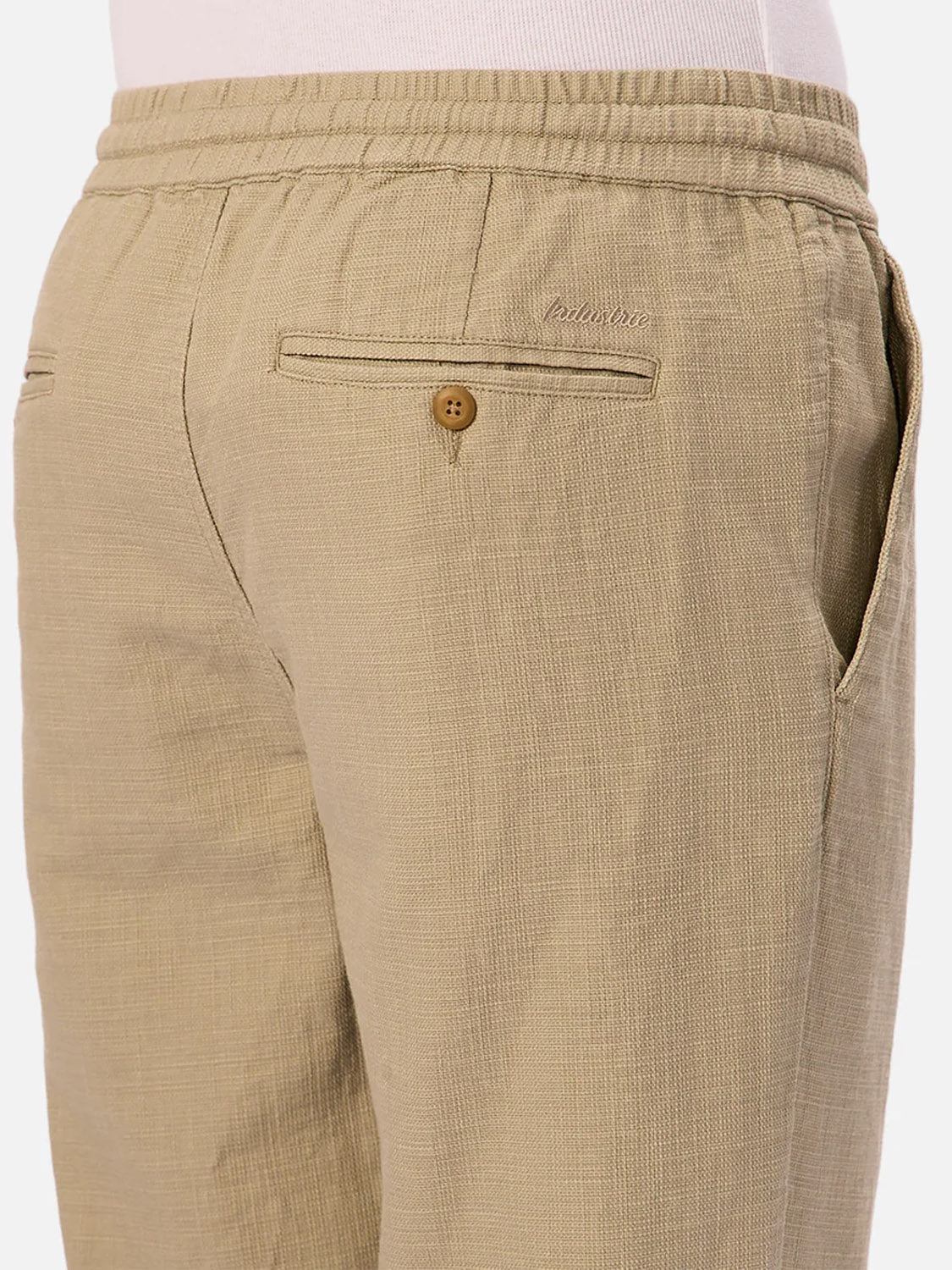 Close-up of the back and side of The Mallorca Pant by Industrie, featuring textured beige cotton, elastic waistband, side pocket, buttoned back pocket, subtle stitching detail, breathable comfort, and a casual fit.