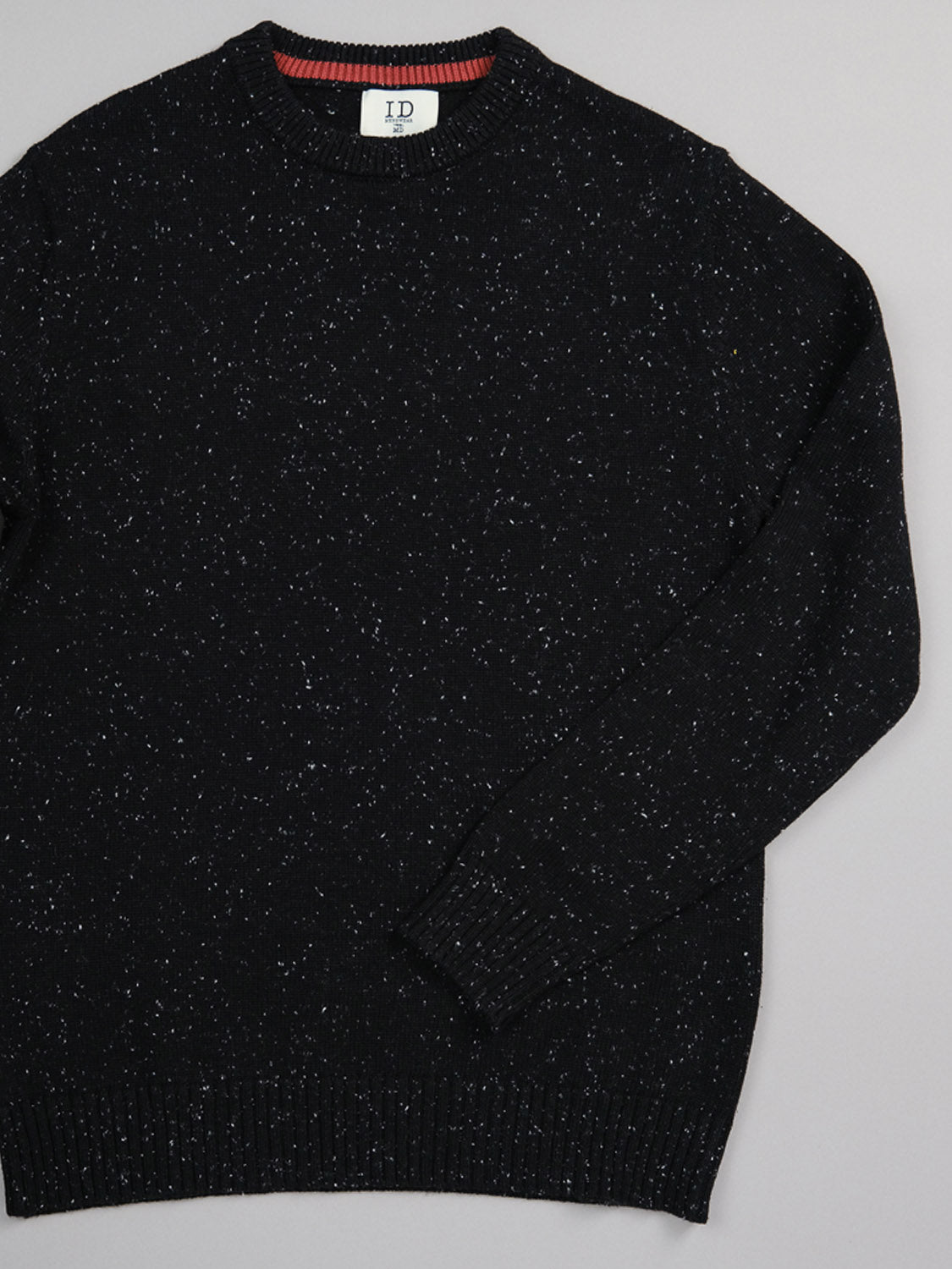 A black speckled Malmo Speckled Cotton Sweater by ID Menswear is displayed on a gray background. It features ribbed crew neck, cuffs, and hem with its inside neck label reading ID bordered by red. This cozy, textured sweater has long sleeves and offers a classic plain knit design.