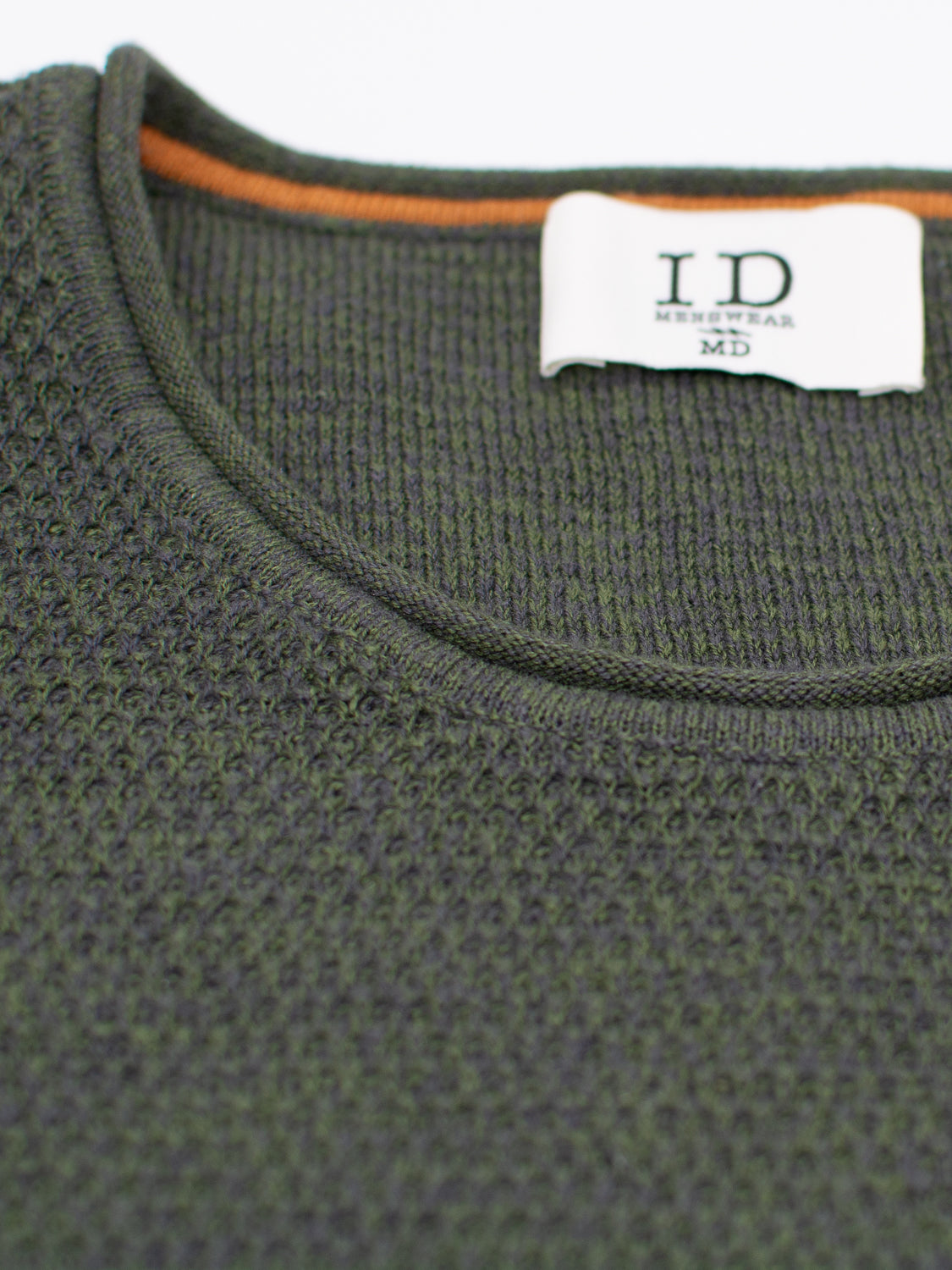 A detailed view of the dark green Malta Rolled Neck Sweater Tee by ID Menswear shows a soft cotton texture. A white label reading I.D MENSWEAR MD is partly visible at the top, and subtle orange trim inside the collar enhances comfort.