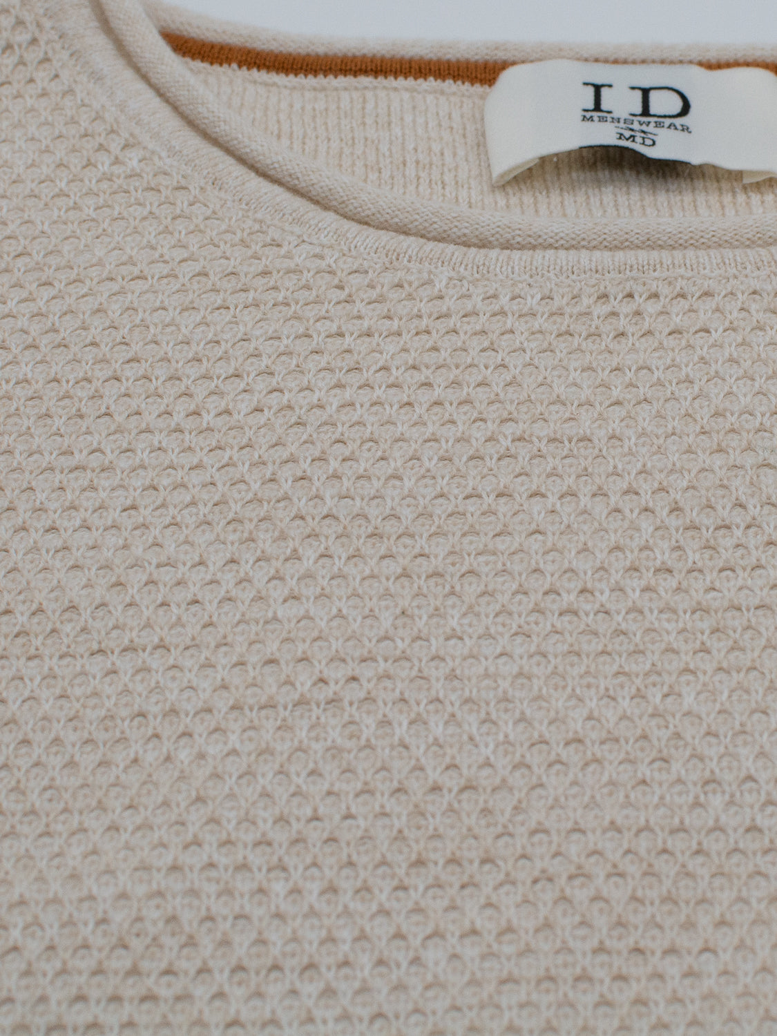 A close-up of the Malta Rolled Neck Sweater Tee shows a beige textured knit and a visible label on the neckline, revealing the brand ID Menswear. Made from soft cotton, it offers a comfortable fit perfect for any occasion.