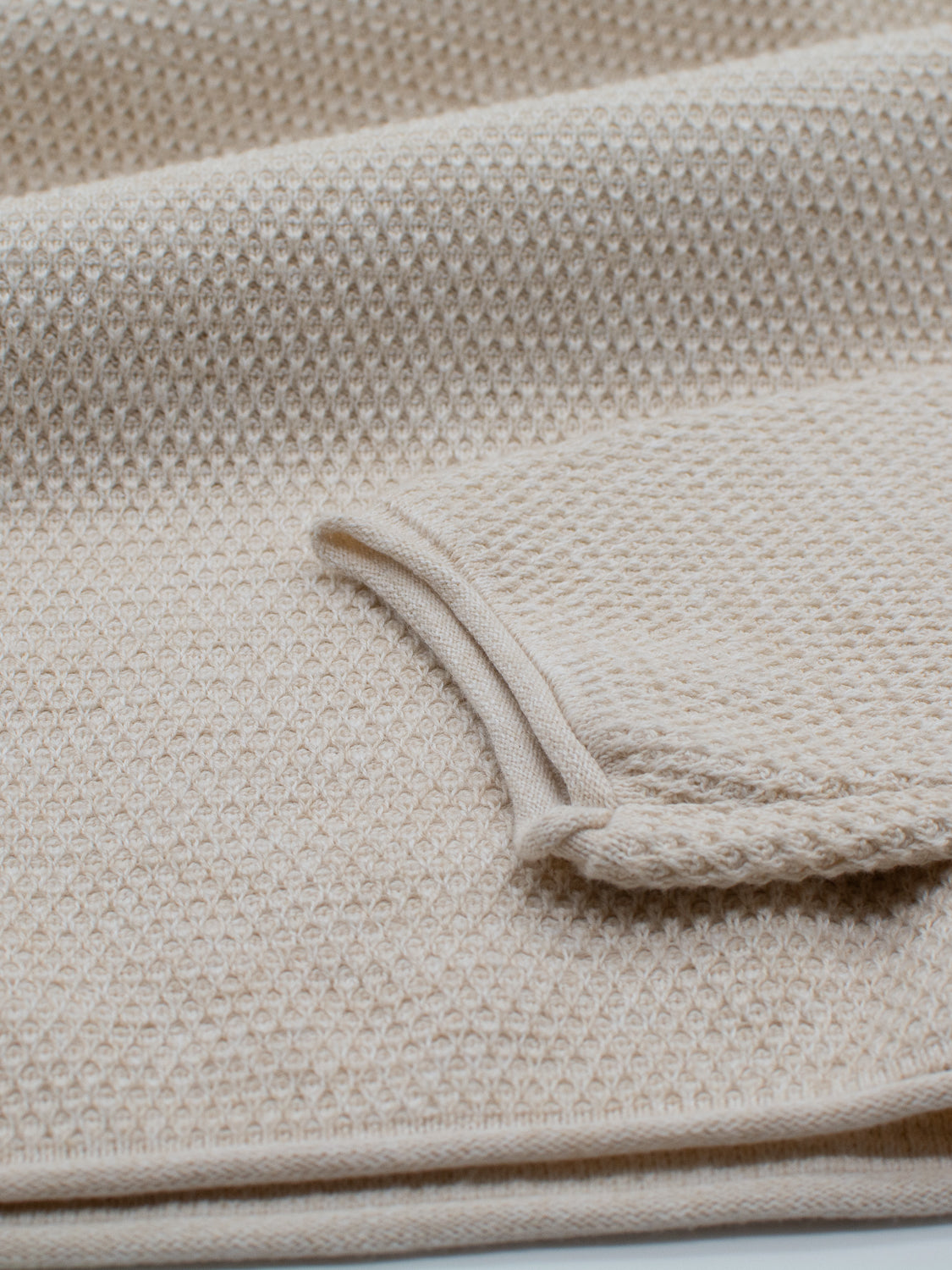 Close-up of a beige waffle-knit fabric with a folded edge, highlighting its texture and knit pattern. Echoing the ID Menswears Malta Rolled Neck Sweater Tee, the image captures the cozy soft cottons warmth and comfortable fit.