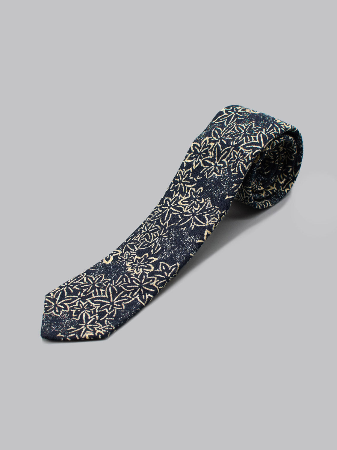The Japanese Printed Maple Tie by ID Menswear, a handmade navy blue necktie with a white floral design, is shown against a plain light gray background.