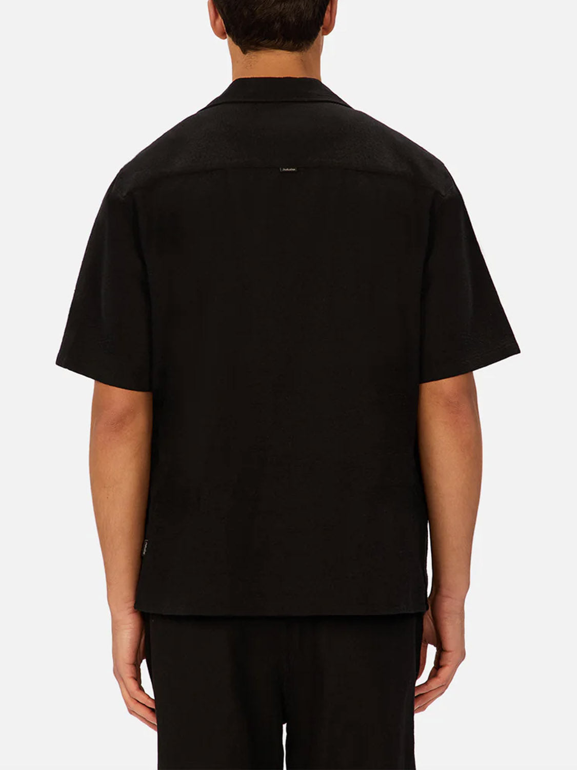 A person faces away from the camera, wearing The Marbella Short Sleeve Shirt by Industrie with matching black pants, set against a plain light background.
