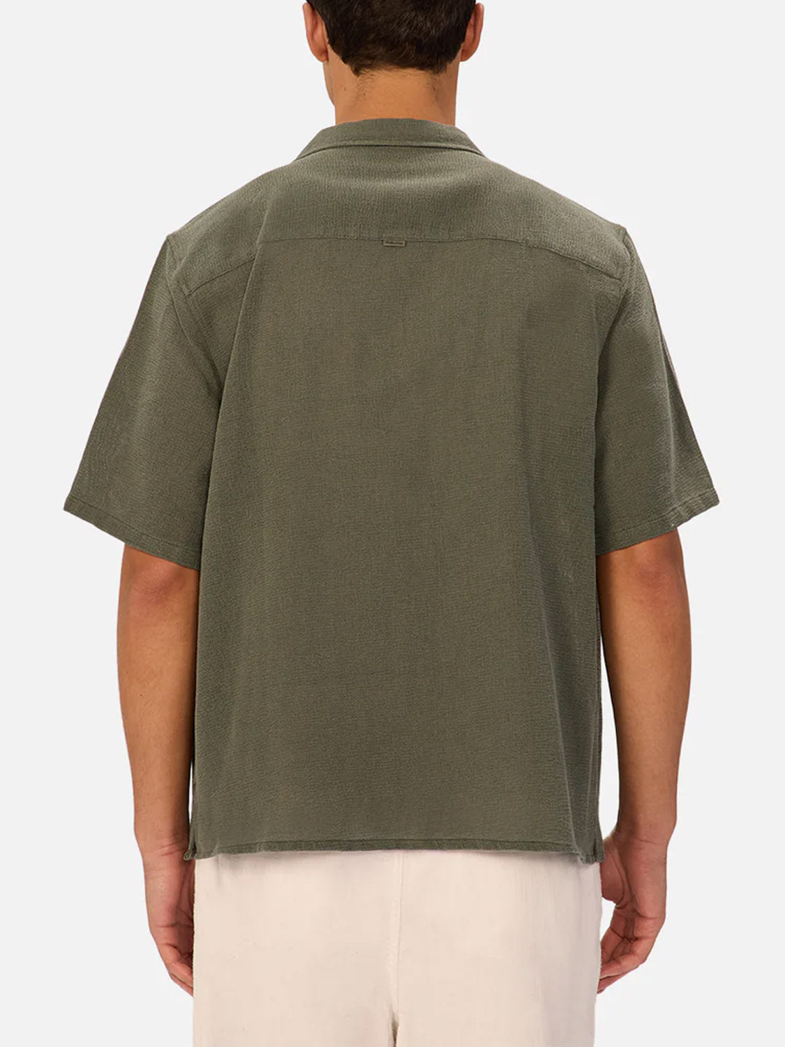 A person is shown from behind wearing Industrie’s The Marbella Short Sleeve Shirt in olive green, made from lightweight, breathable fabric, paired with light-colored shorts against a plain background.