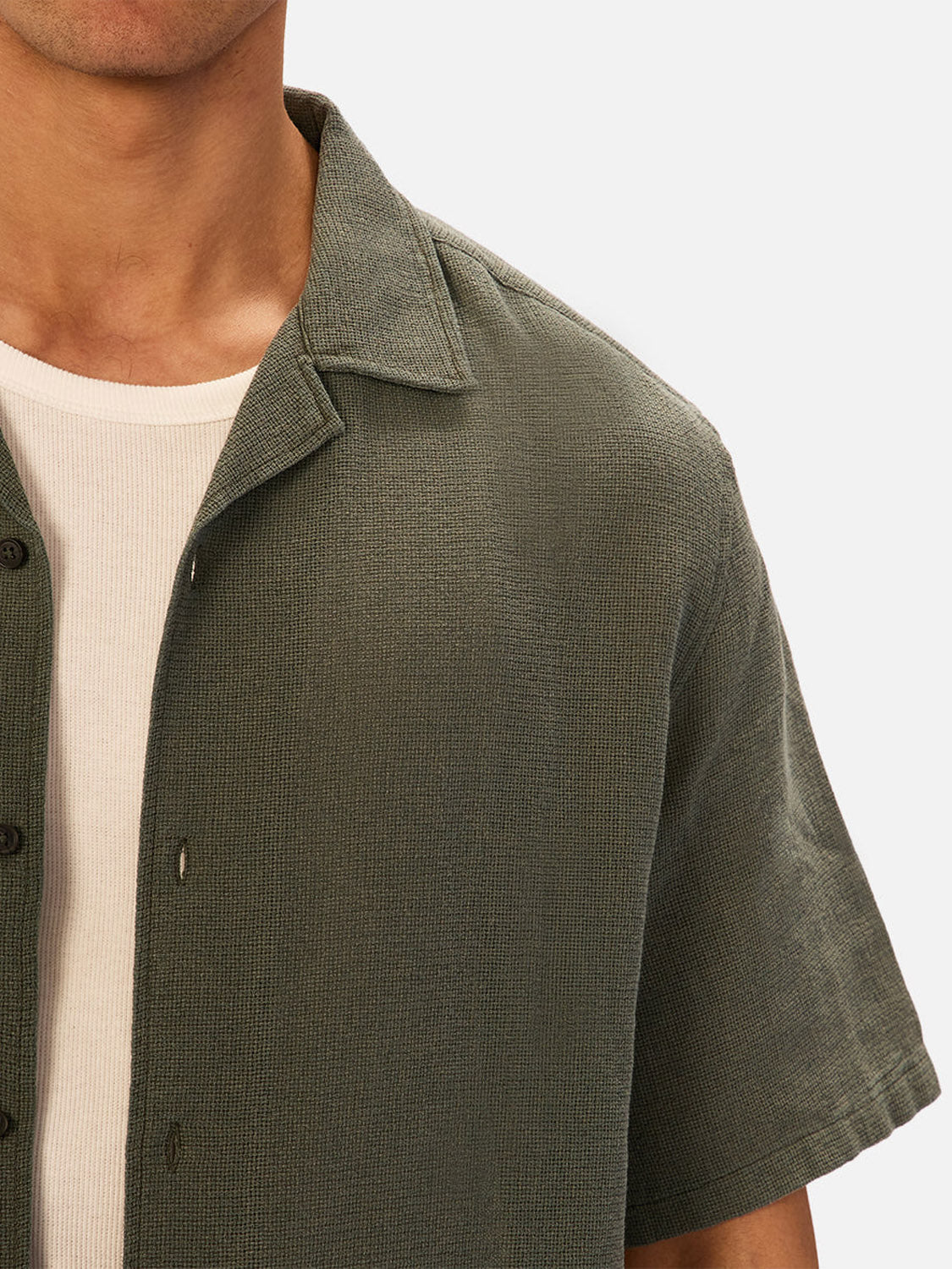 A close-up of a person wearing Industrie’s The Marbella Short Sleeve Shirt in olive green, featuring lightweight textured fabric, layered over a white ribbed crew-neck tee, shown from shoulders to mid-torso.