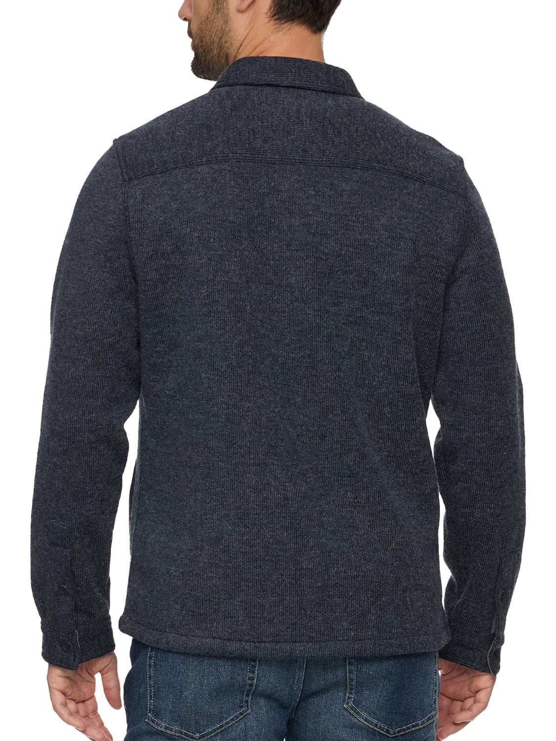 A man with short dark hair and a trimmed beard is seen from the back wearing Flag and Anthem's Mason Fleece Lined Shirt Jacket in dark blue with textured fabric, buttoned cuffs, and blue jeans.