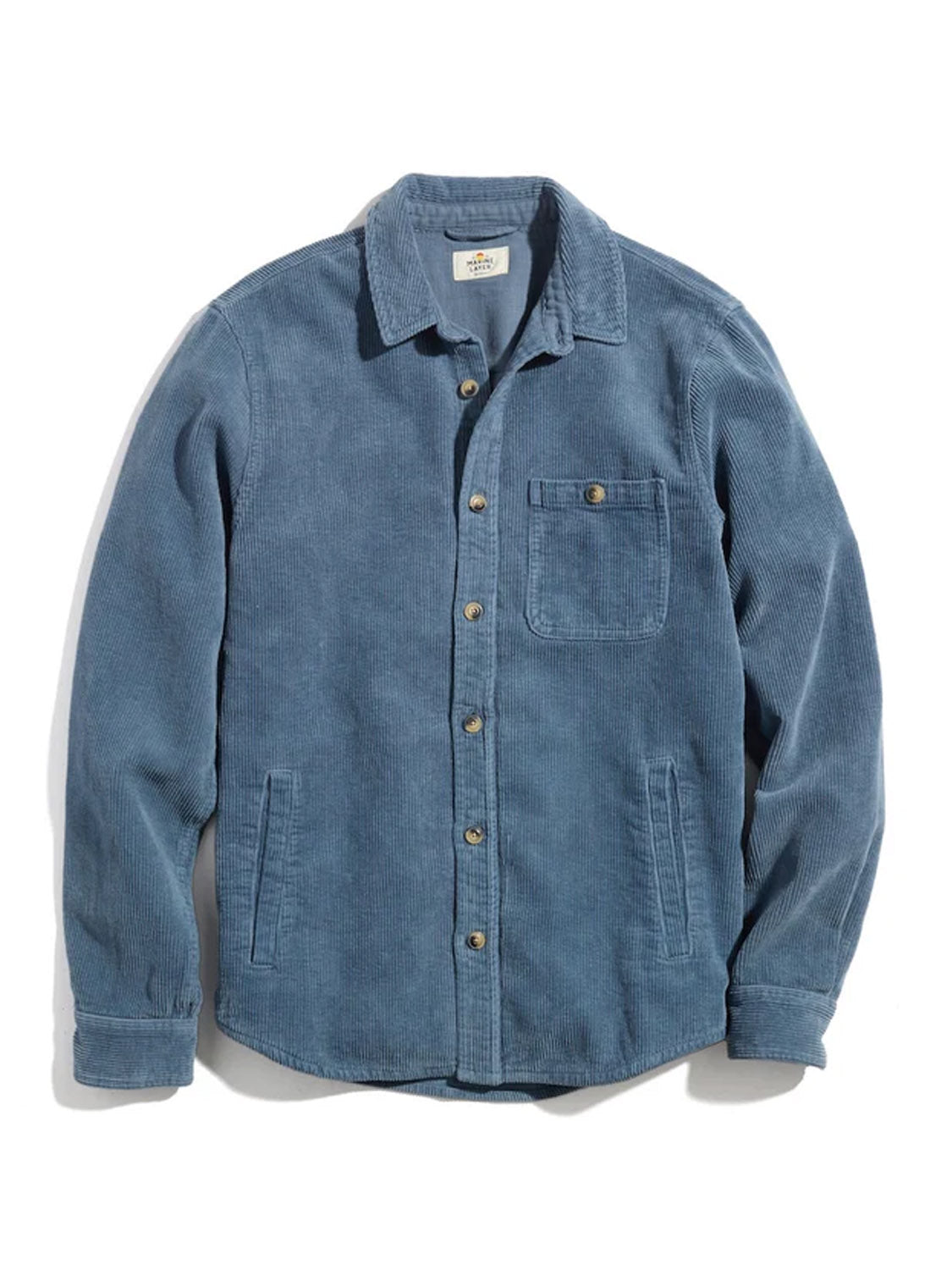 The Marine Layer Max Broken In Corduroy Overshirt, a blue 8-wale corduroy piece with a button-up front, includes a single buttoned chest pocket and two side pockets. Its textured ribbed fabric provides a classic look. The shirt is showcased flat on a white background.