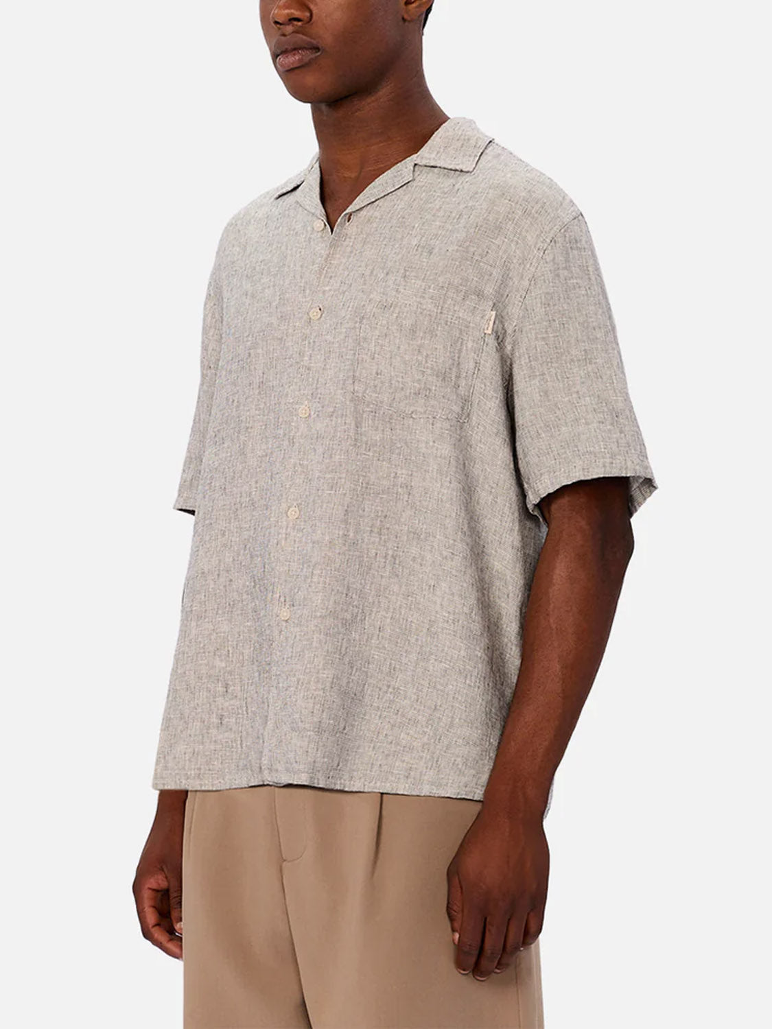 A man wears the Industrie Melrose Short Sleeve Shirt in light grey with a collar and loose fit, paired with light brown pants, standing against a plain light background.