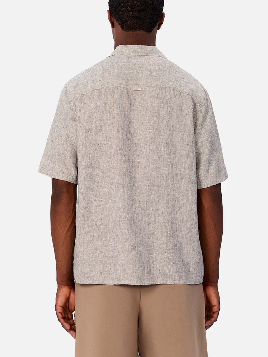 A man is seen from behind wearing the Industrie Melrose Short Sleeve Shirt in light grey, featuring a relaxed fit and straight hem, paired with tan shorts. The textured shirt’s soft drape stands out against the light background.