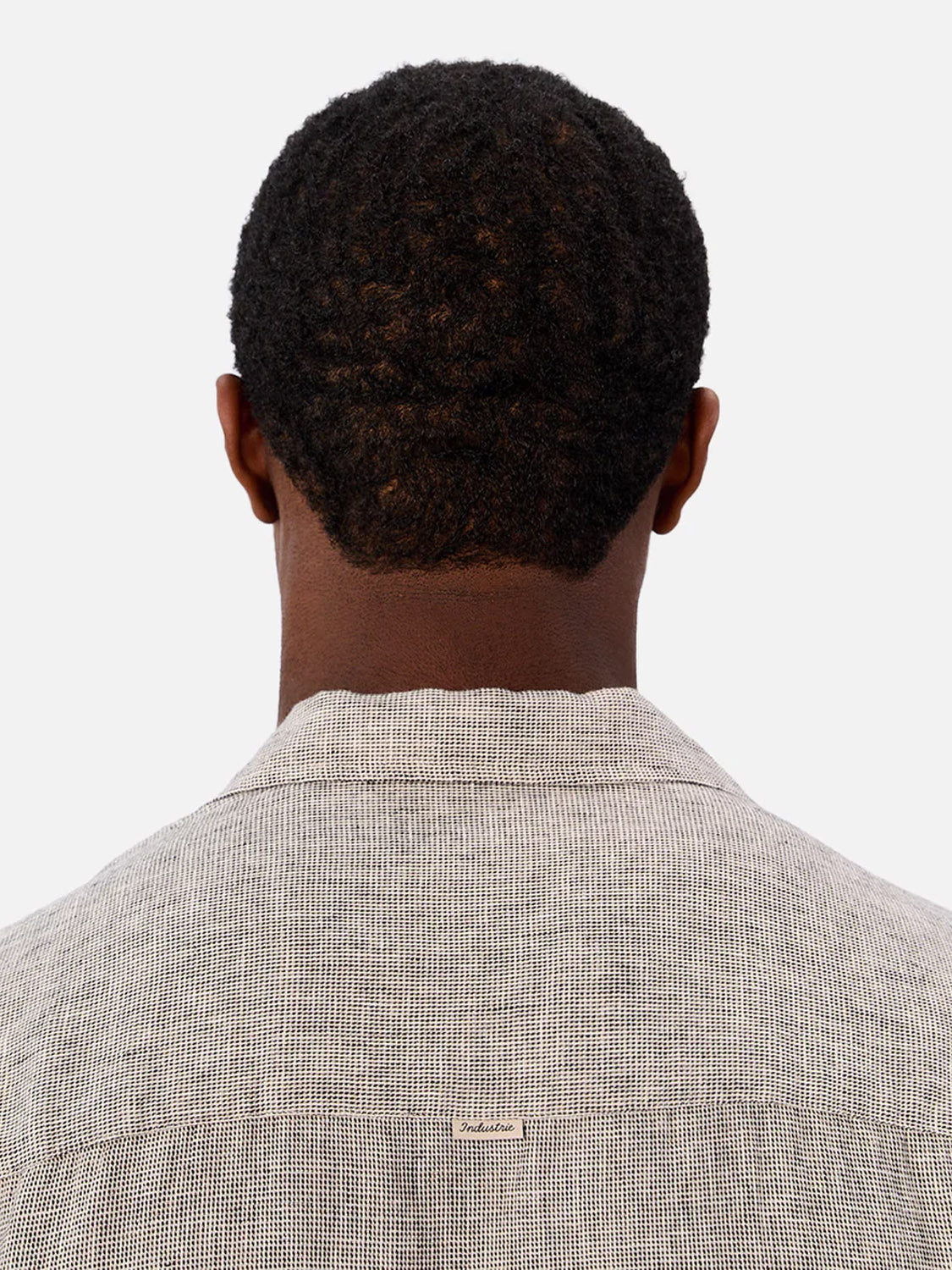 A person with short, curly hair is seen from behind wearing the Industrie Melrose Short Sleeve Shirt in light gray with a subtle houndstooth pattern and a small white collar tag. The background is plain white.