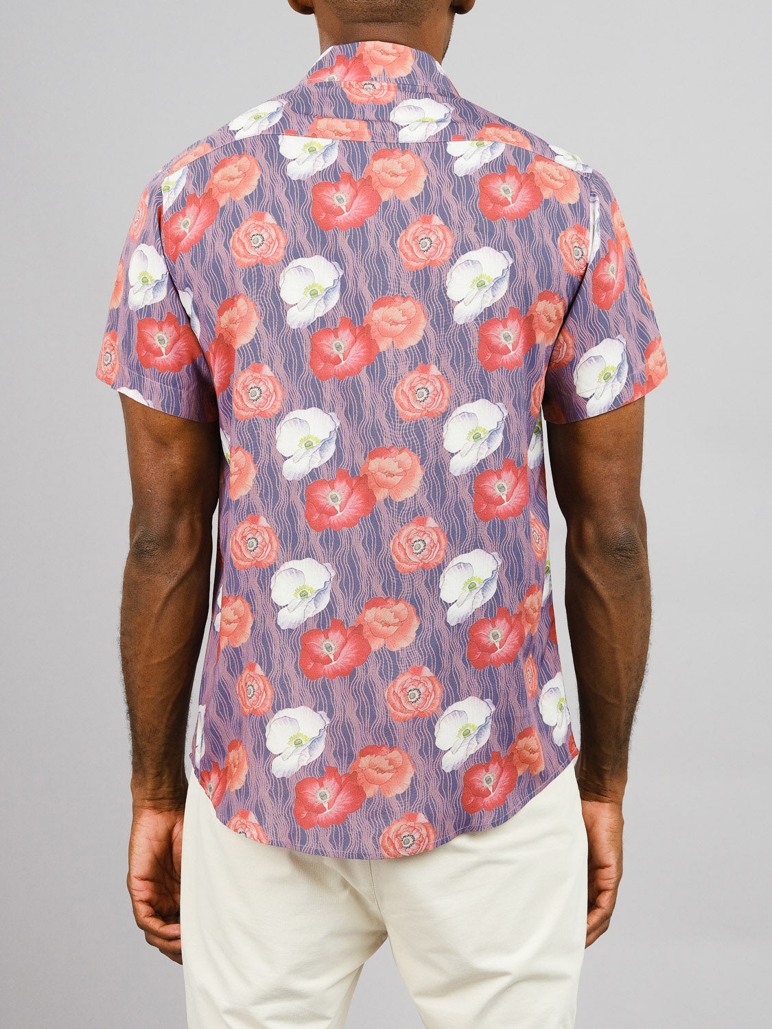 A person stands with their back to the camera wearing the Metok Printed Rayon Shirt by ID Menswear, featuring vibrant red, white, and orange floral prints. Paired with light pants against a gray backdrop—ideal for warm weather.
