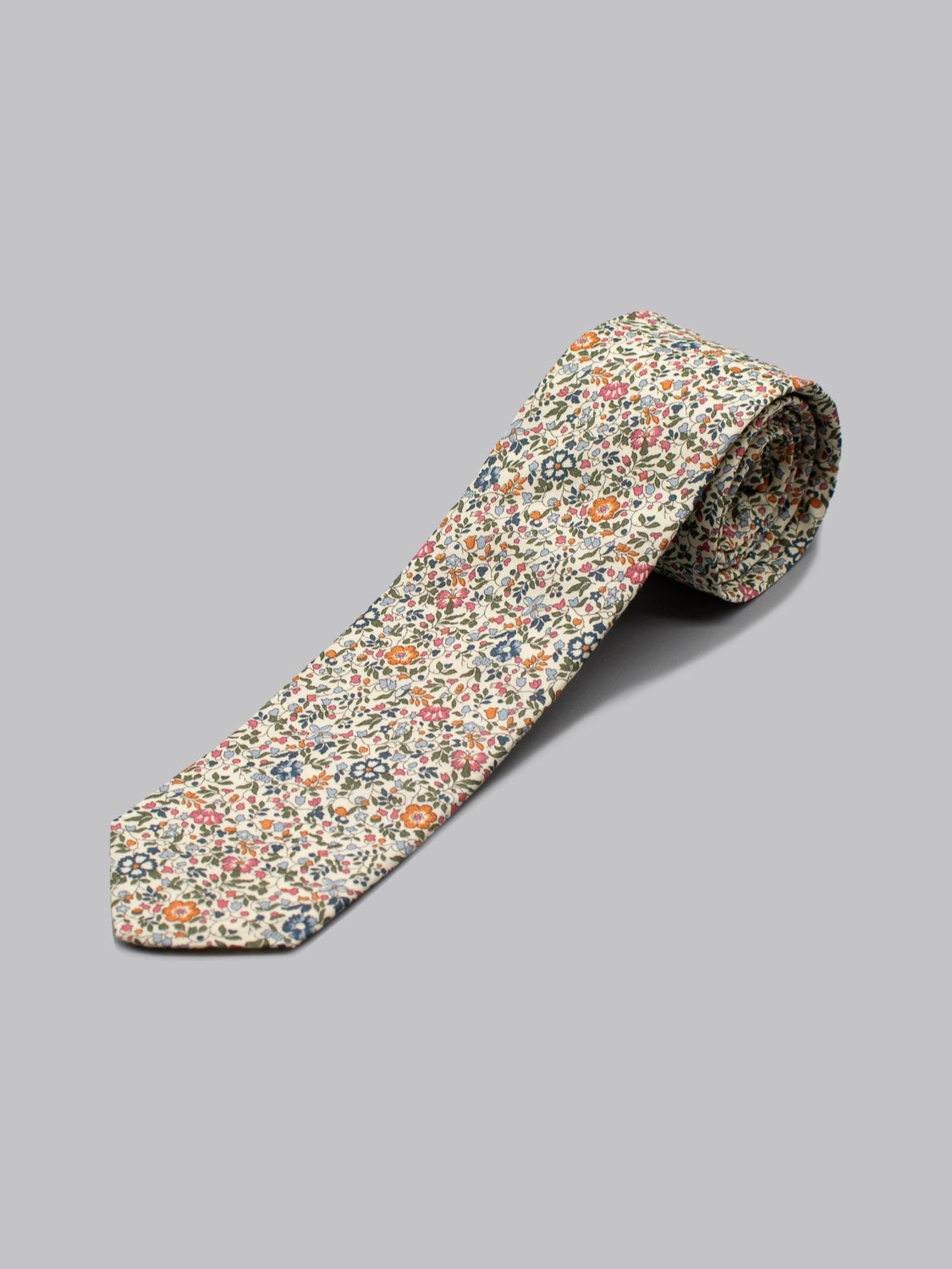 A rolled-up ID Menswear Liberty of London Tana Lawn™ Millie tie, featuring a multicolored floral print on cotton and handmade in Brooklyn, displayed on a plain gray surface.