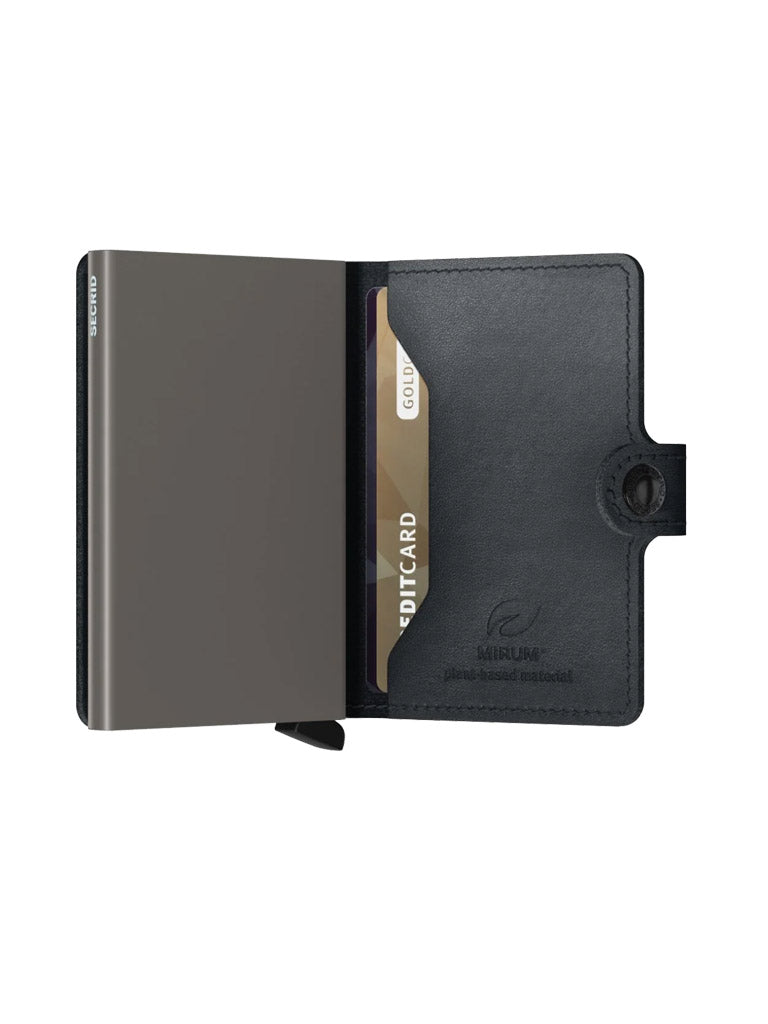 A black Secrid Miniwallet Mirum with a flap open reveals a slim, gray compartment and a partially visible gold card. The wallet offers RFID protection, a button closure, and has the NILIUM logo embossed on the inner flap.
