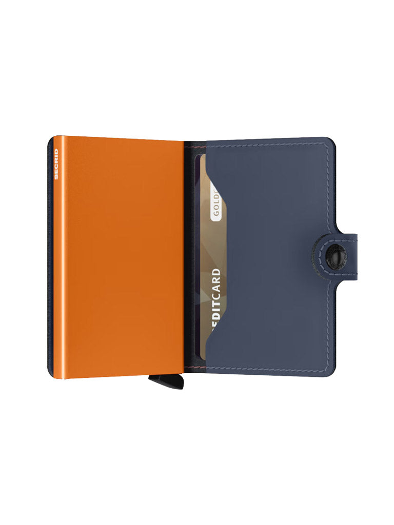 The Secrid Miniwallet Matte Finish Leather in navy blue is open, displaying an orange interior and a gold credit card partially visible in a slot with its compact design and snap closure.
