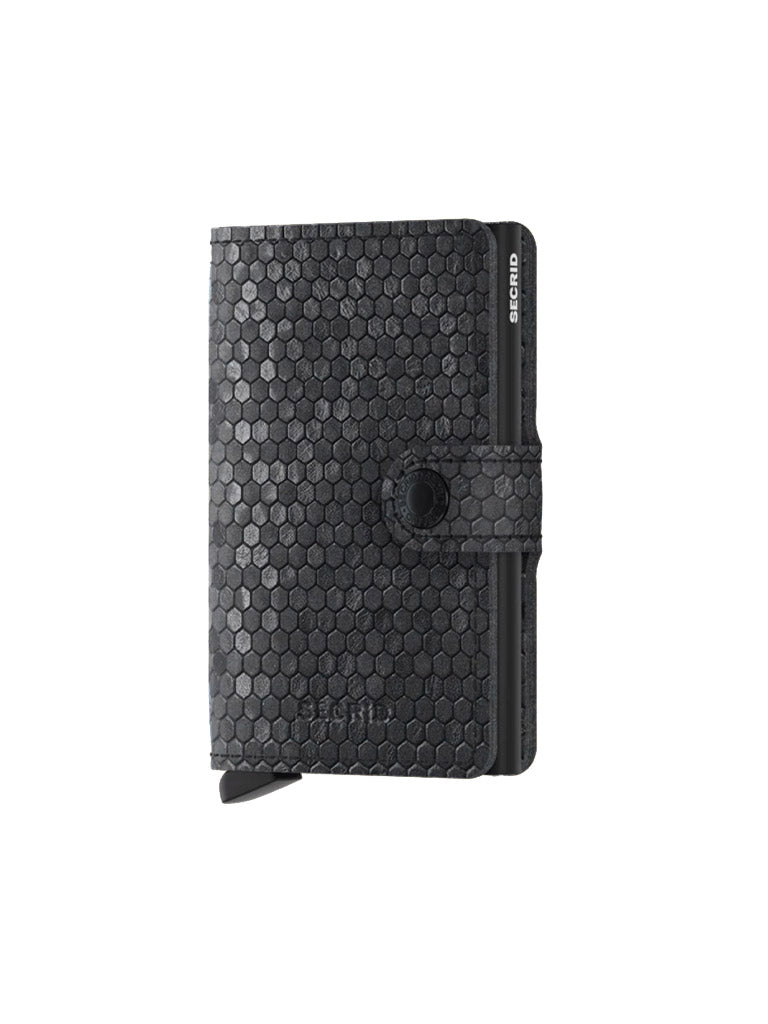 The Secrid Miniwallet Hexagon is a black leather wallet with a hexagonal pattern, RFID protection, buttoned strap closure, and a small bottom tab, shown on a plain white background.