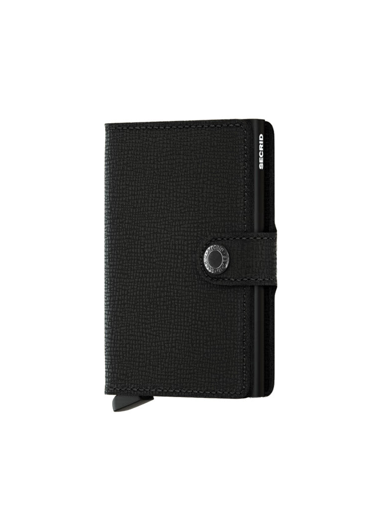 The Secrid Miniwallet Crisple by Secrid is a black textured leather wallet with RFID protection, snap-button closure, and a small tab at the bottom left. SECRID appears in white on the upper right edge. The wallet is shown standing upright on a white background.