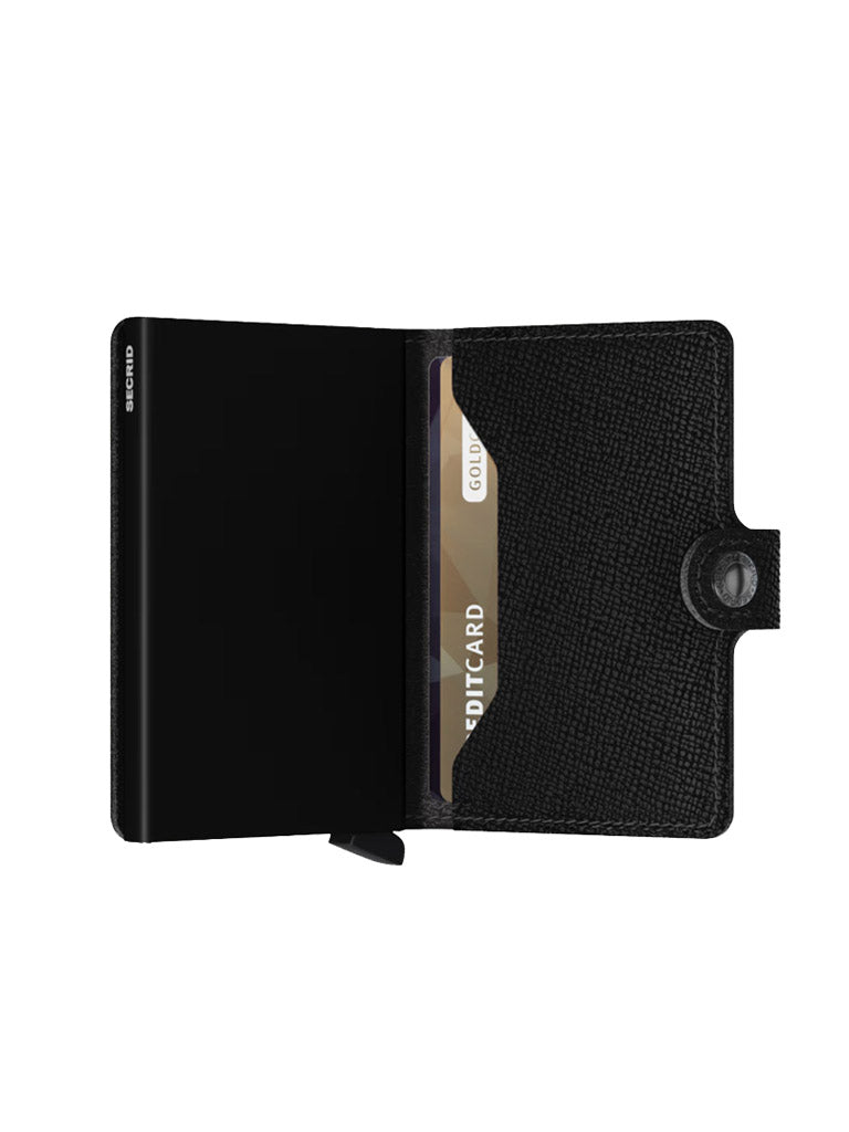 The Secrid Miniwallet Crisple, made of black textured leather, is open to reveal card slots and a partially visible gold and white credit card. It features RFID protection and a snap button closure on the right.