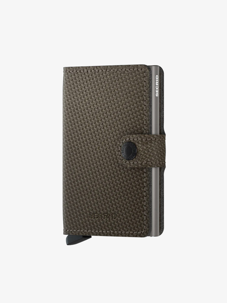 The Secrid Miniwallet Carbon Weave Pattern Leather is a textured brown RFID/NFC-secure wallet with a black snap strap, metal edges, and bottom lever, shown against a plain white background.