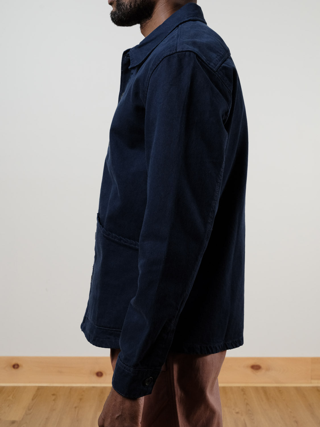 A person stands indoors, facing left, wearing the !SOLID Nadil Cotton Button-Up Overshirt in navy blue with brown pants, posed neutrally against a light wall and wooden floor.