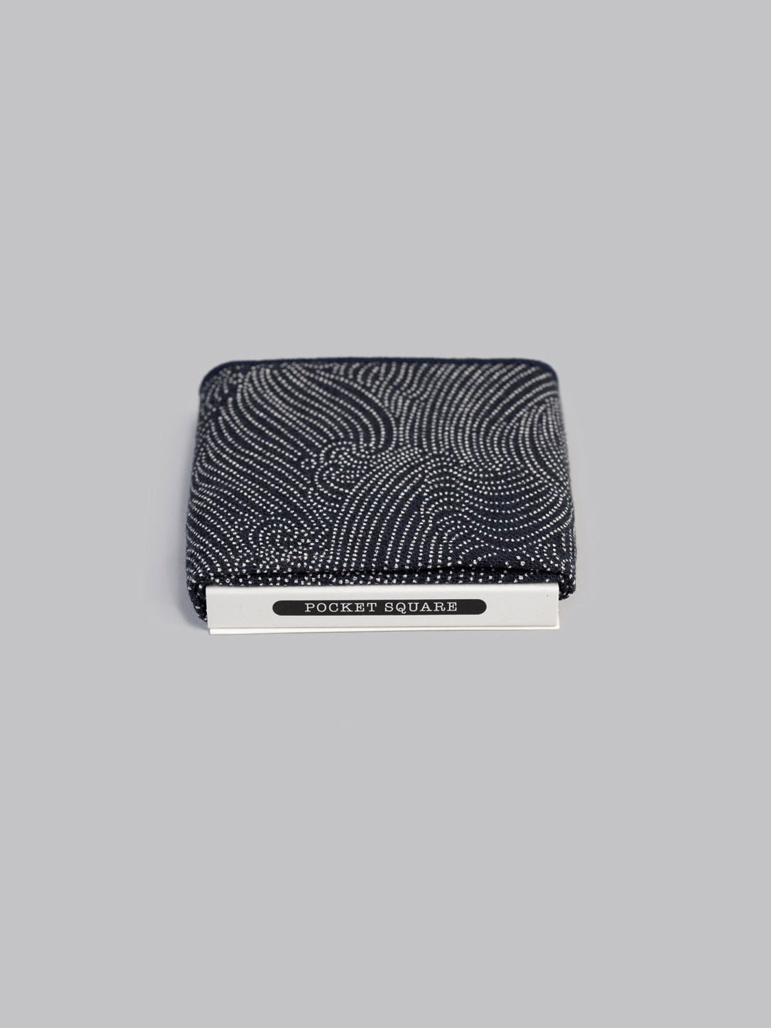 The Nami Pocket Square by ID Menswear, a handmade black cotton square with white dots and a POCKET SQUARE label, is shown against a plain gray background.
