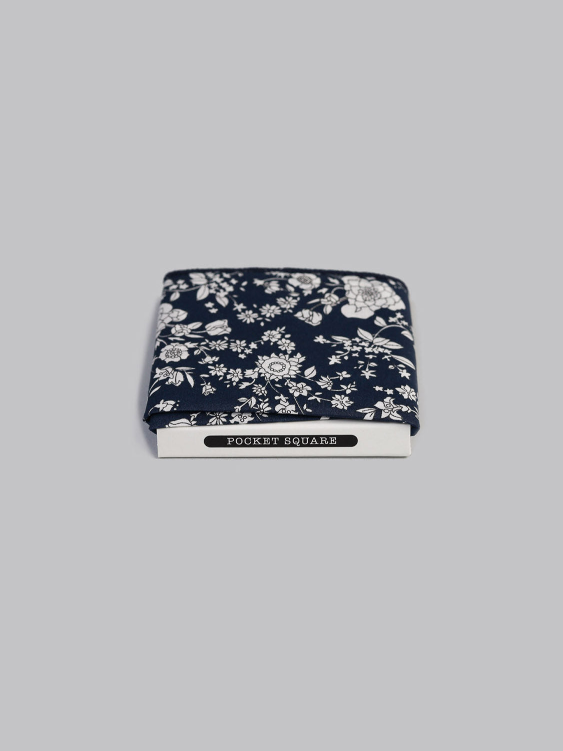 The Liberty™ Navy Lawn Pocket Square by ID Menswear, made from Tana Lawn cotton with a white floral pattern, comes neatly folded in packaging labeled Pocket Square and is shown on a plain light gray background.