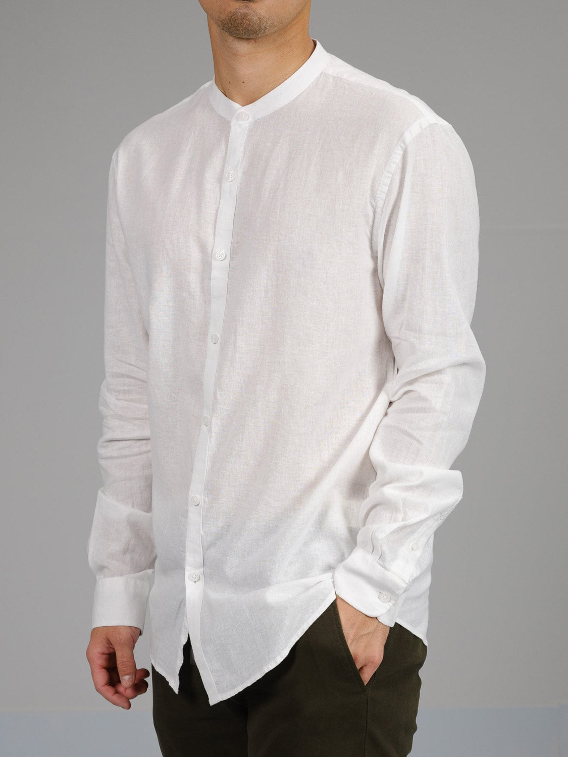 A person is wearing the Nehru Linen Cotton Mandarin Collar Shirt by ID Menswear, a white long-sleeve button-up made of a breathable linen cotton blend, with dark pants. They stand against a plain gray background, arms relaxed by their sides.