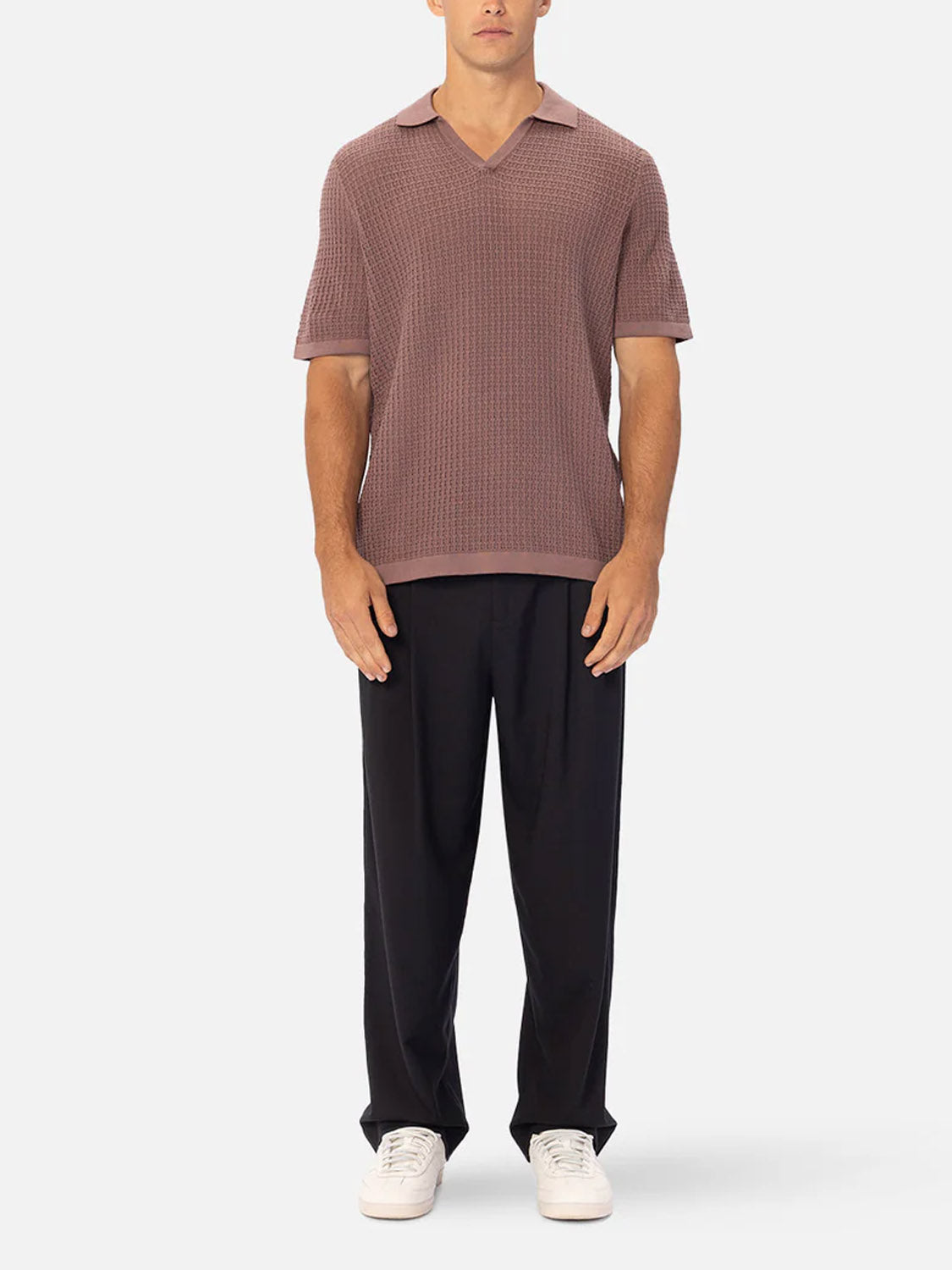 A man faces forward wearing a short-sleeve, textured mauve polo shirt, Industrie’s The New Milano Pants - Loose Fit, and white sneakers against a plain light gray background.