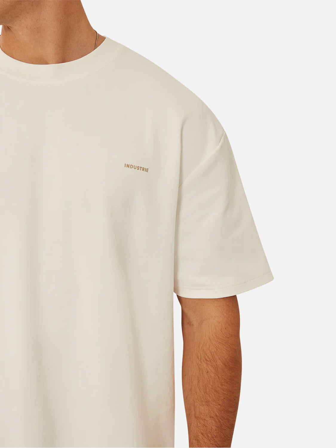 A person wears The Newport T-Shirt by Industrie, a plain off-white heavyweight crew neck with short sleeves and subtle "INDUSTRIE" branding on the left chest. Only the upper half of their body is visible.